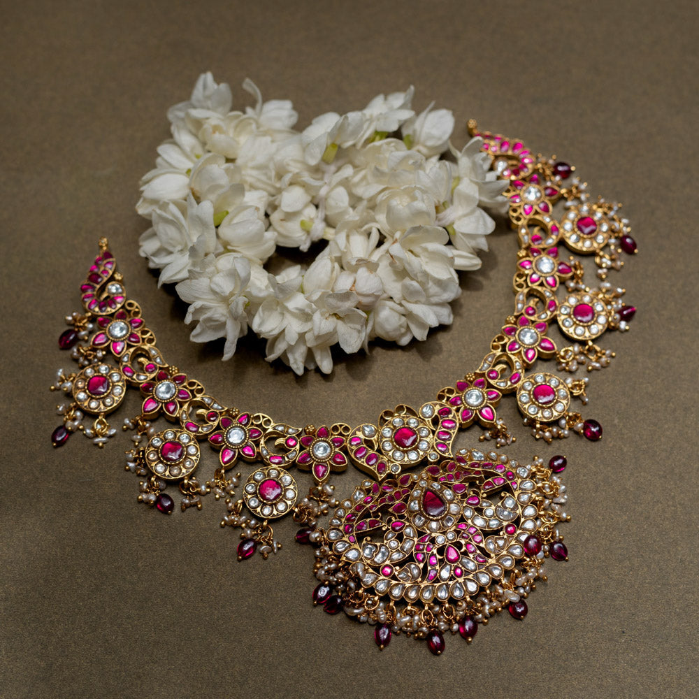 A handcrafted 22ct gold-plated 92.5 sterling silver Rani Haar Kemp Necklace, featuring red, green, and white Kundan stones, red beads, and pearls, with a long, multi-stranded design, intricate floral motifs, and a central pearl-clustered pendant, ideal for bridal ensembles and festive occasions.