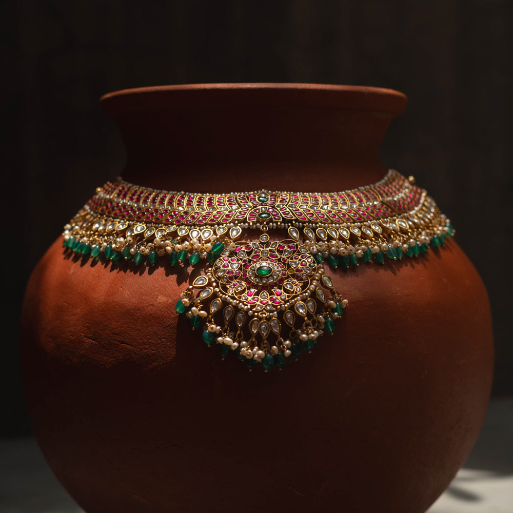 A handcrafted 22ct gold-plated 92.5 sterling silver Rajsi Kemp Choker, featuring red, green, and white Kundan stones, red beads, and pearls, with a broad, ornate design and a central pearl-clustered pendant, ideal for bridal wear and grand celebrations.