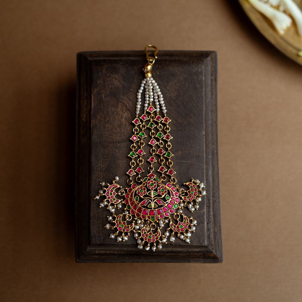 A floral tikka with green and red Kundan stones and dangling pearls.