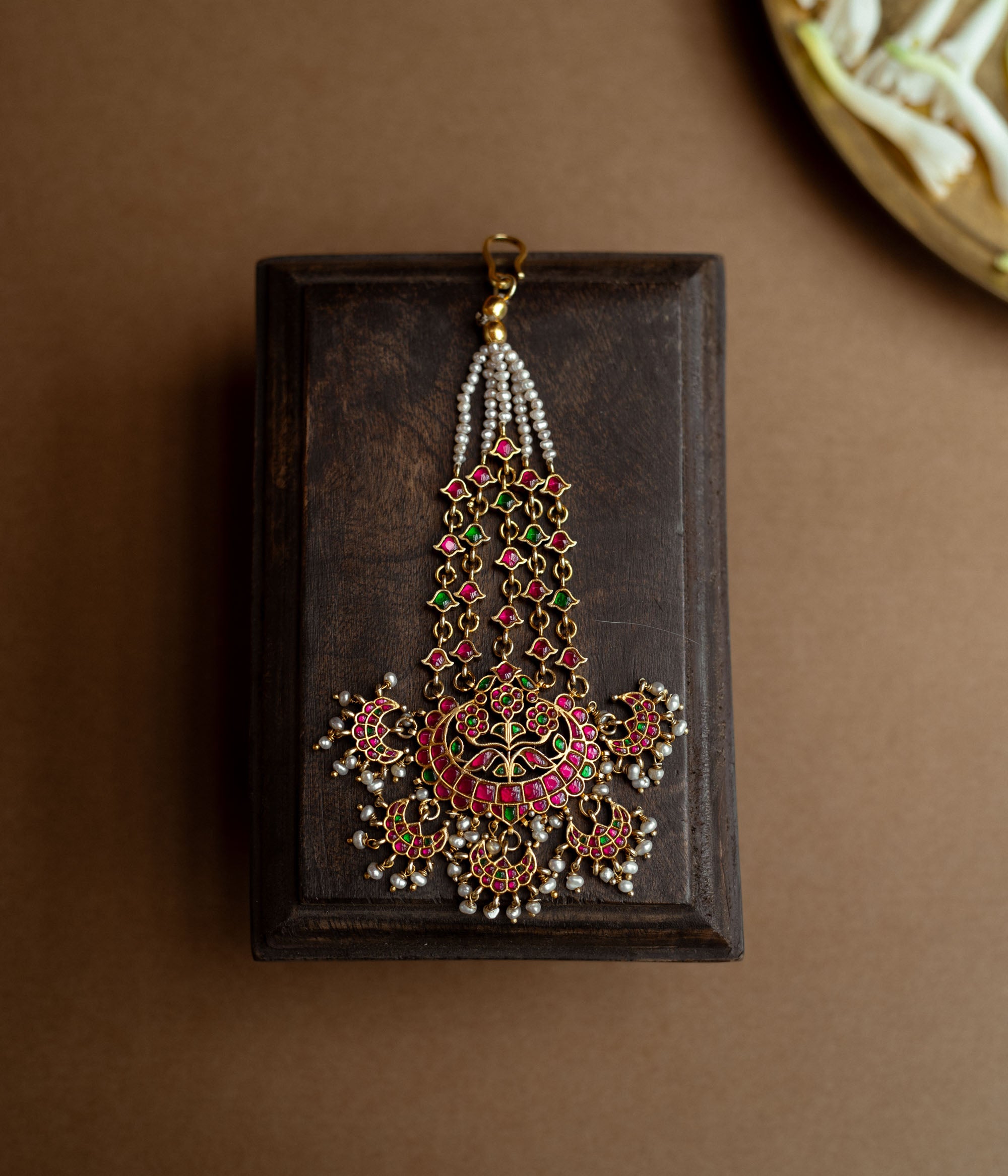 A floral tikka with green and red Kundan stones and dangling pearls.