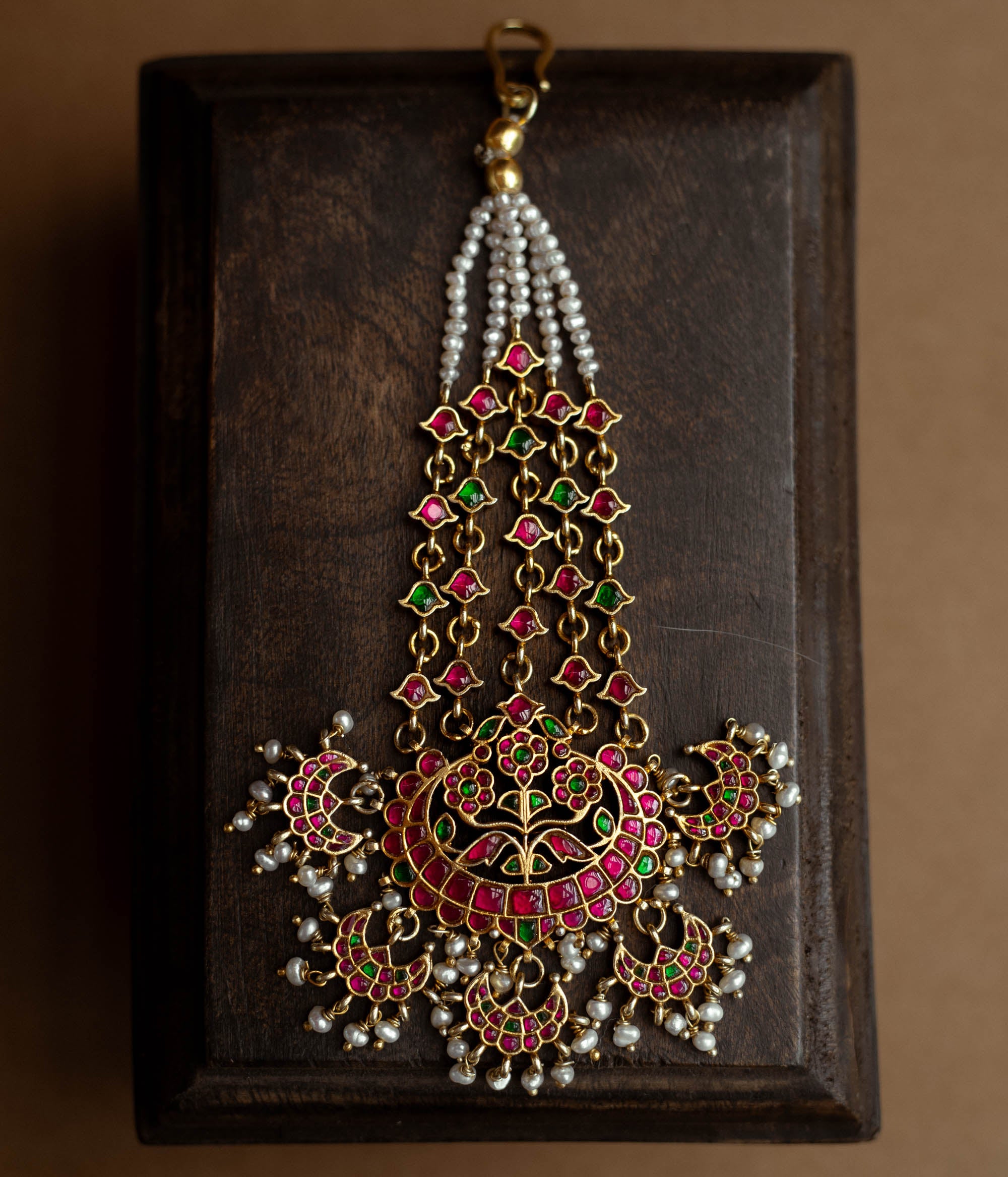A floral tikka with green and red Kundan stones and dangling pearls.