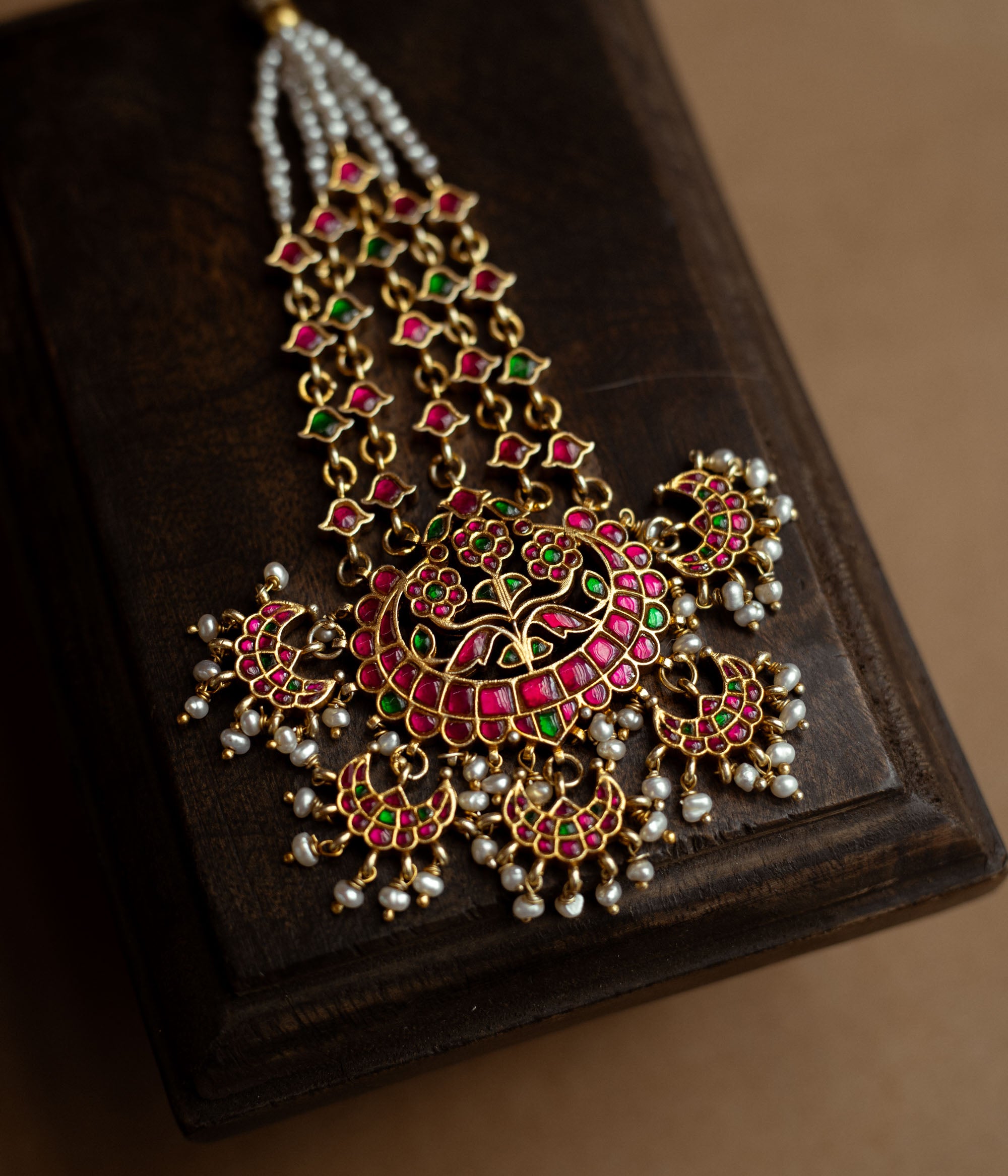 A floral tikka with green and red Kundan stones and dangling pearls.