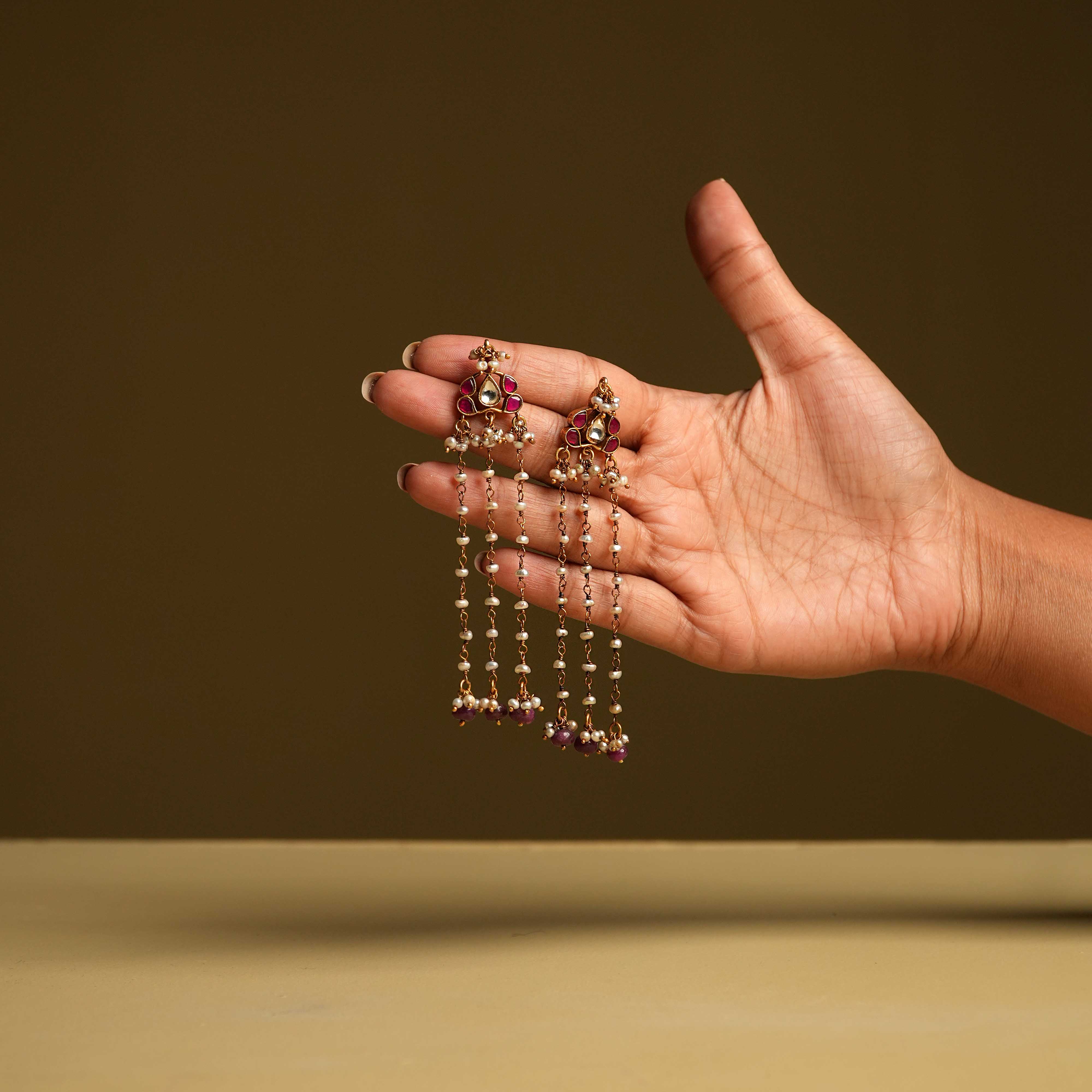Keshini Earrings made of 92.5 sterling silver with screw-type fastening. Featuring red and white Kundan stones, red beads, and pearls, this exquisite pair exudes celestial elegance and timeless charm, designed for the woman who captivates with every glance.