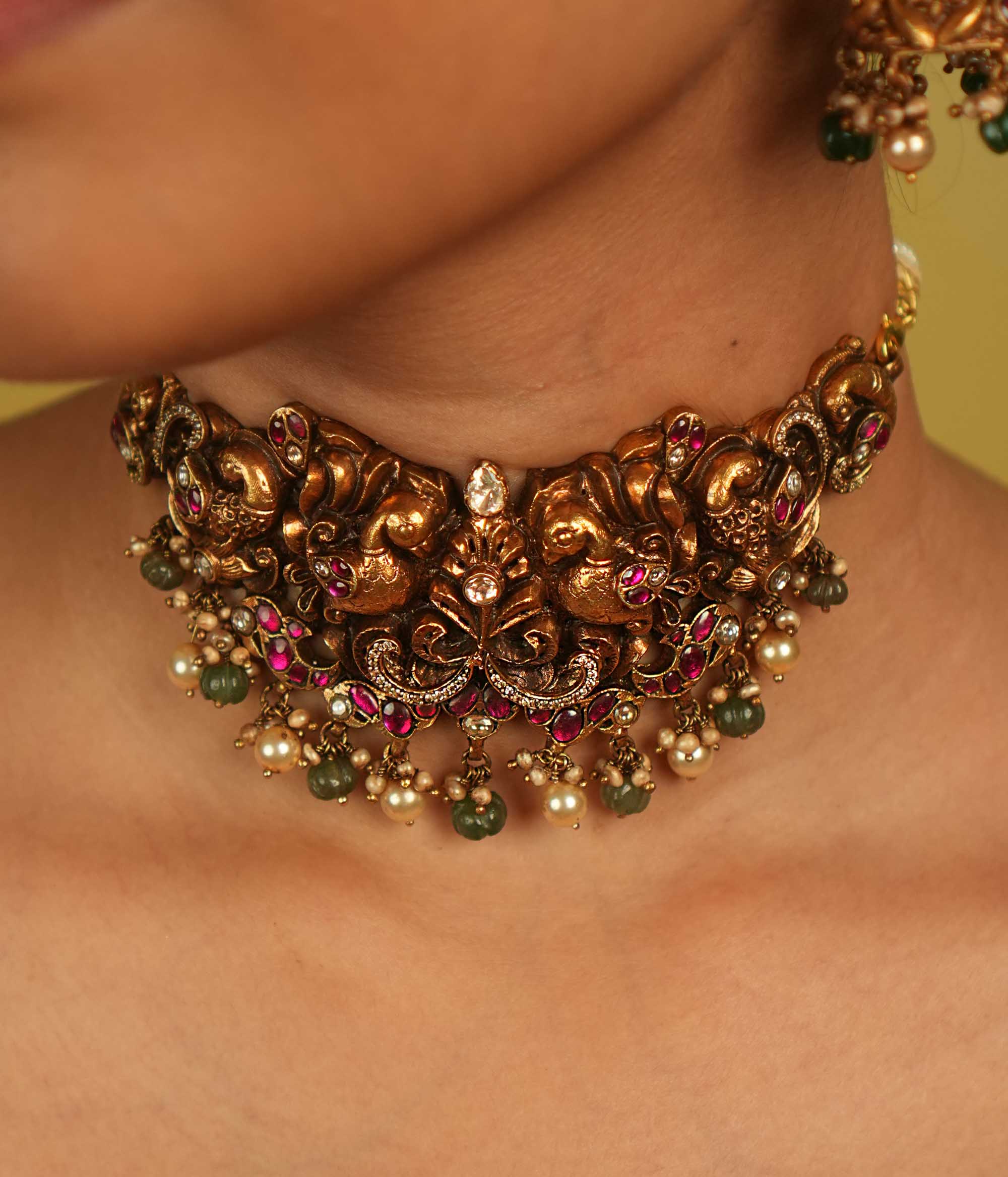A peacock-inspired choker adorned with red, white, and green kundan, polki, and CZ stones, with delicate green and white bead droplets. More than an adornment, it is a timeless tribute to culture and divine beauty.