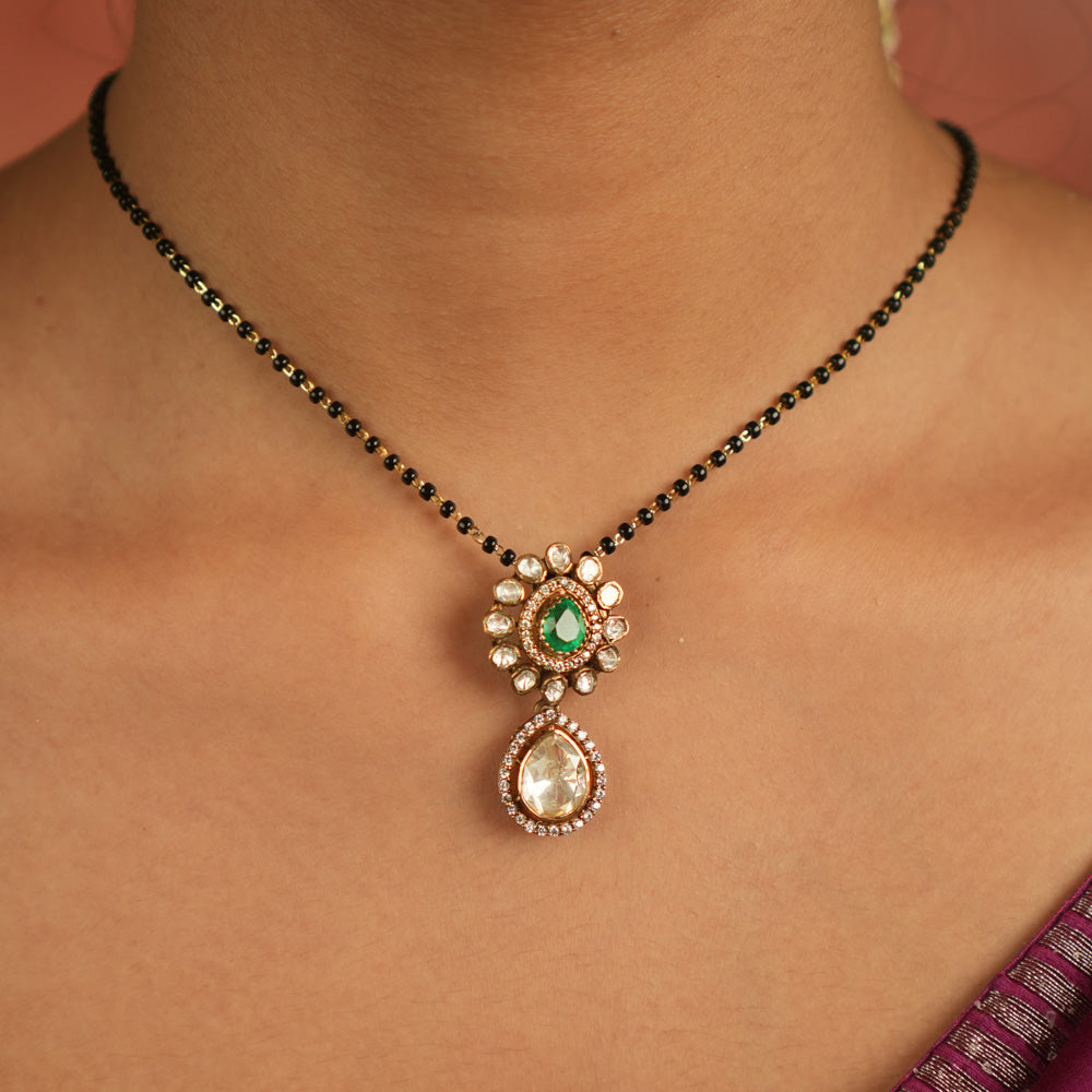 An enchanting floral pendant adorned with Moissanite Polki stones and a vibrant green gemstone at its heart, encircled by shimmering CZ stones—nature’s grace reborn, a dewdrop of timeless elegance.