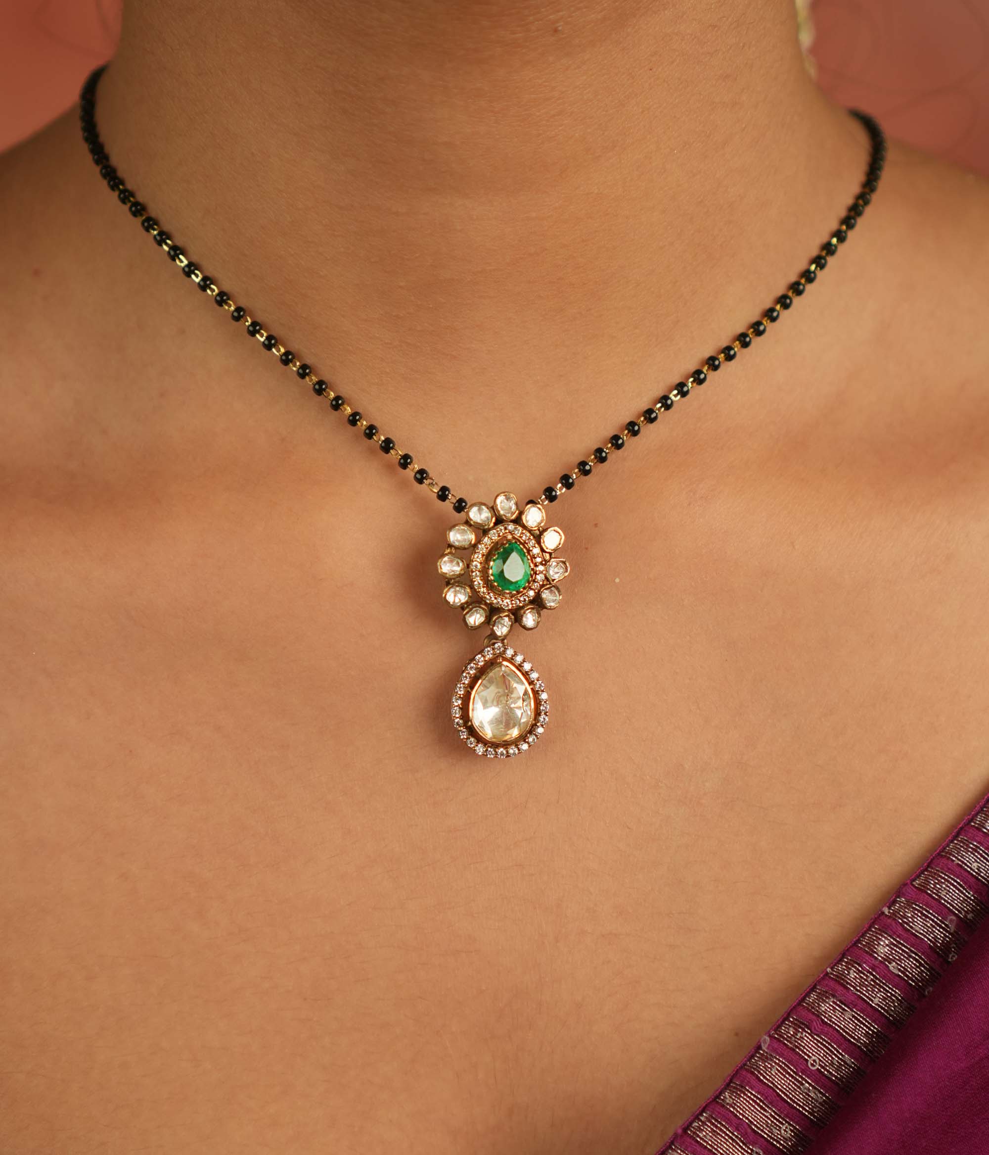 An enchanting floral pendant adorned with Moissanite Polki stones and a vibrant green gemstone at its heart, encircled by shimmering CZ stones—nature’s grace reborn, a dewdrop of timeless elegance.