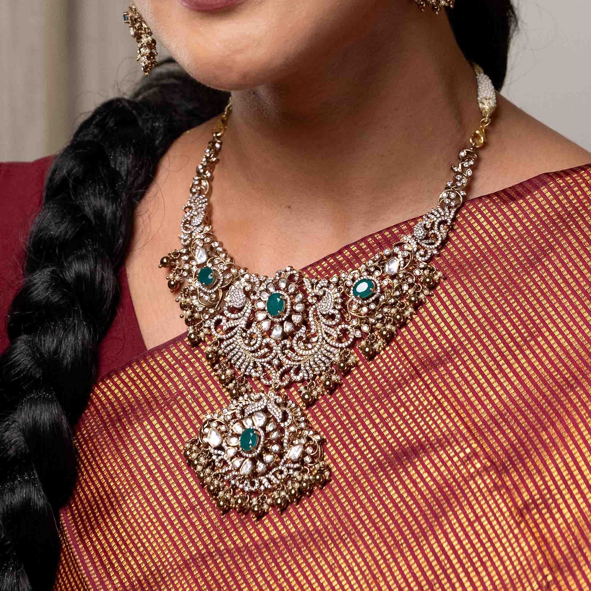 Close-up of a person wearing a decorative necklace with emerald green stones on a red saree.