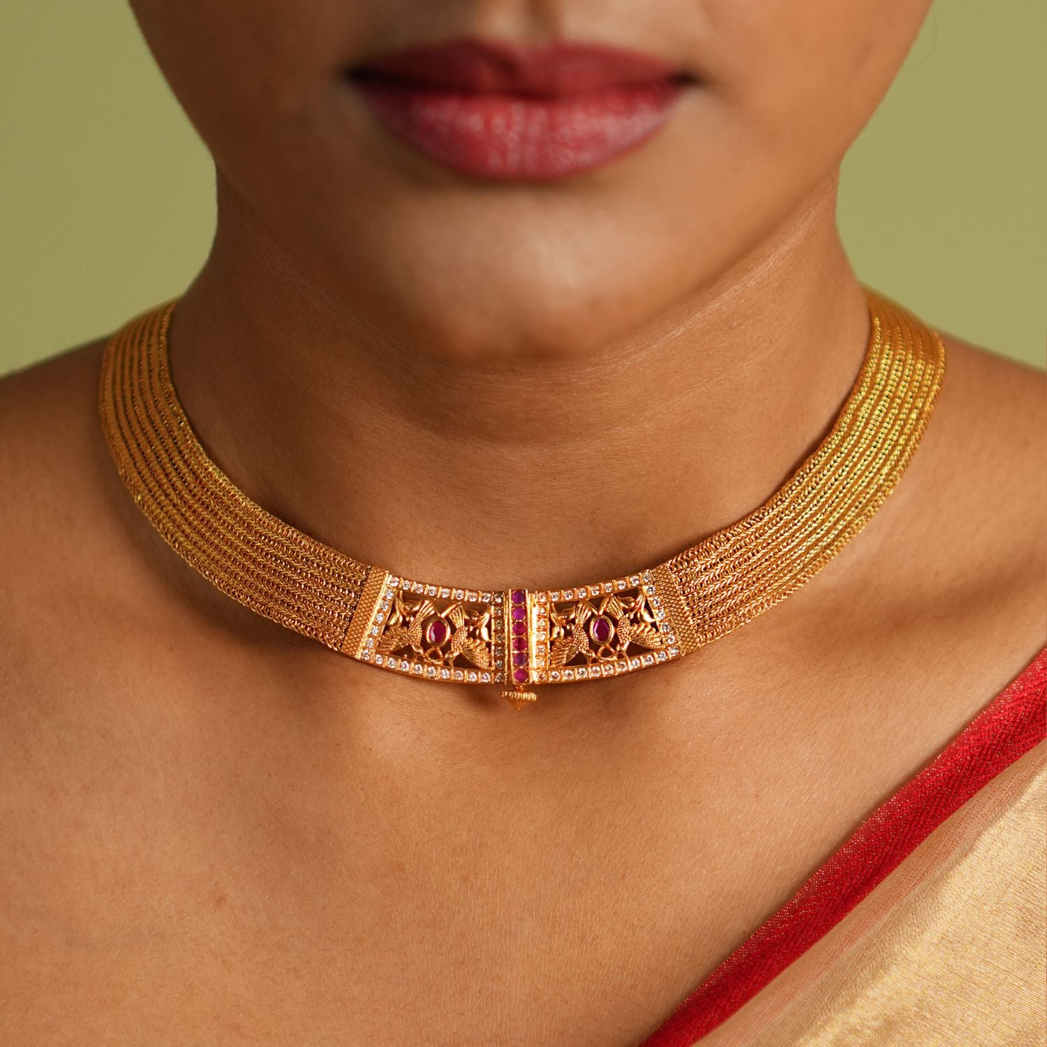 Elegant gold-plated silver necklace featuring a continuous flat-structured chain with a secure screw closure at the end. The design is adorned with intricate tiny peacock motifs, embellished with vibrant red Kundan stones and shimmering CZ stones, adding a touch of traditional grace and sophistication.