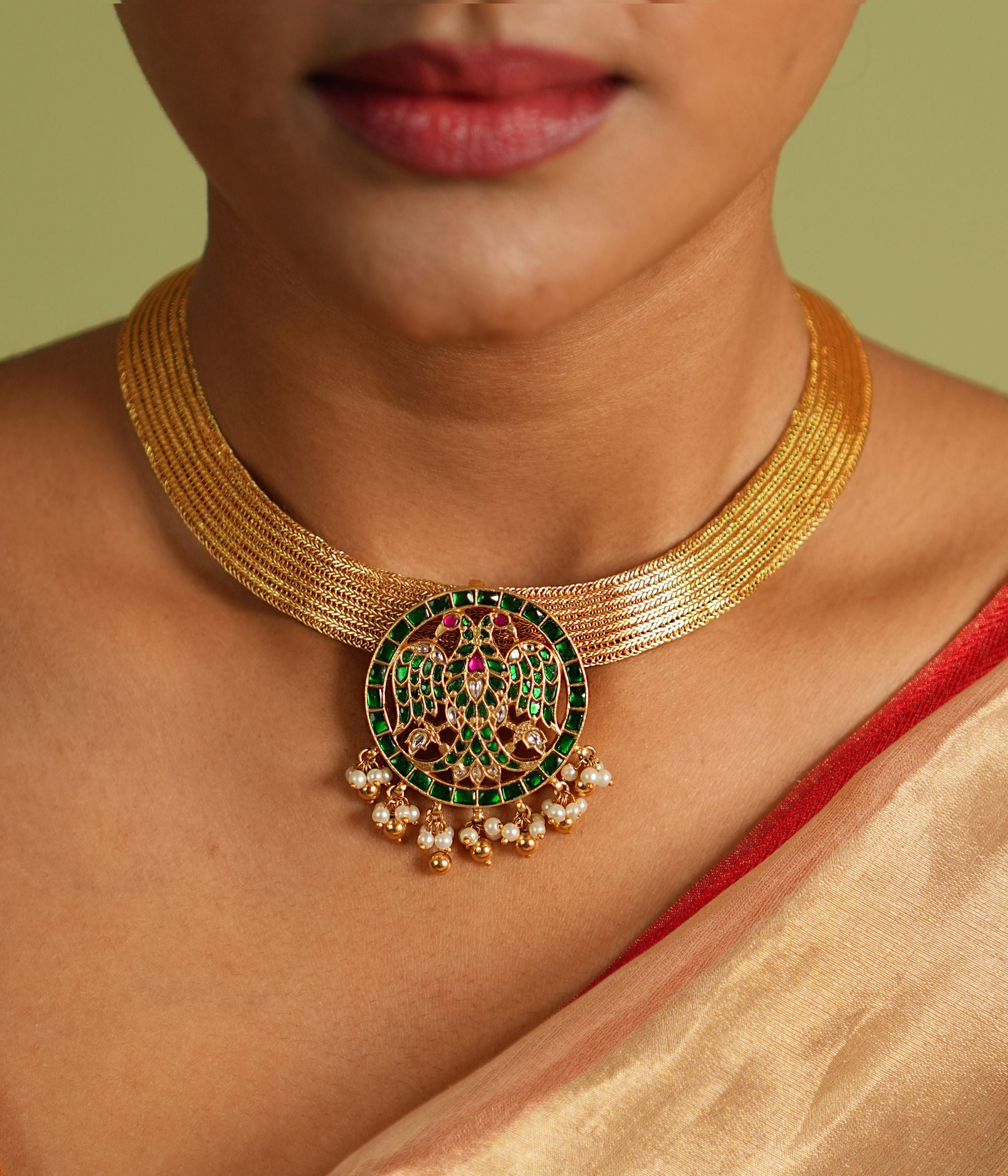 Elegant gold-plated silver necklace featuring a continuous flat-structured chain with a secure screw closure at the end. The design is adorned with intricate tiny peacock motifs, embellished with vibrant red Kundan stones and shimmering CZ stones, adding a touch of traditional grace and sophistication.