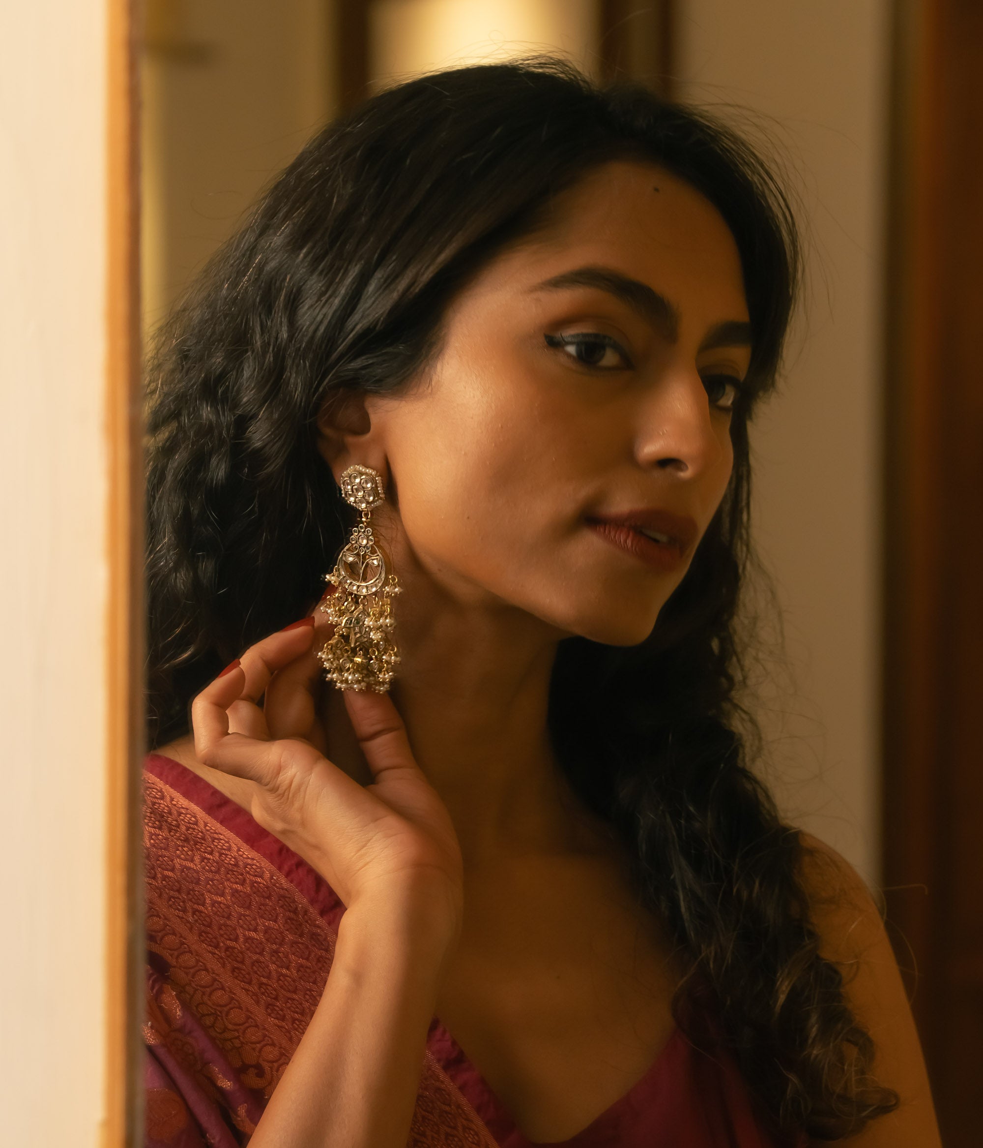 Woman wearing ornate gold Taarini earrings with rubies, white sapphires, and pearl danglers.