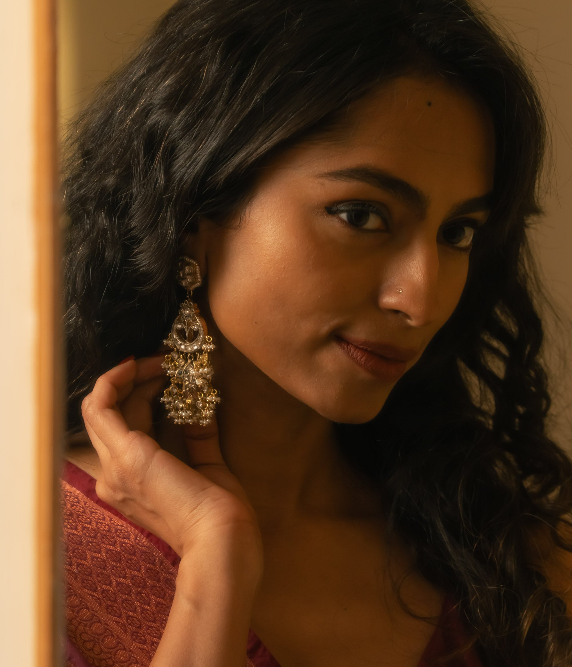 Woman wearing ornate gold Taarini earrings with rubies, white sapphires, and pearl danglers.