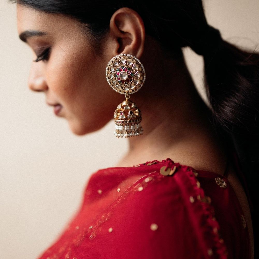 Large gold jhumka earrings with white sapphires, rubies, and pearls, on a woman wearing a red sari.