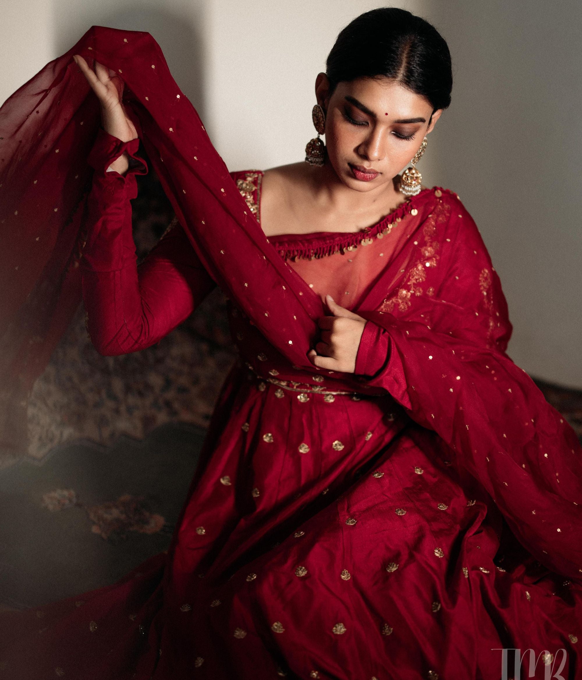 Large gold jhumka earrings with white sapphires, rubies, and pearls, on a woman wearing a red sari.