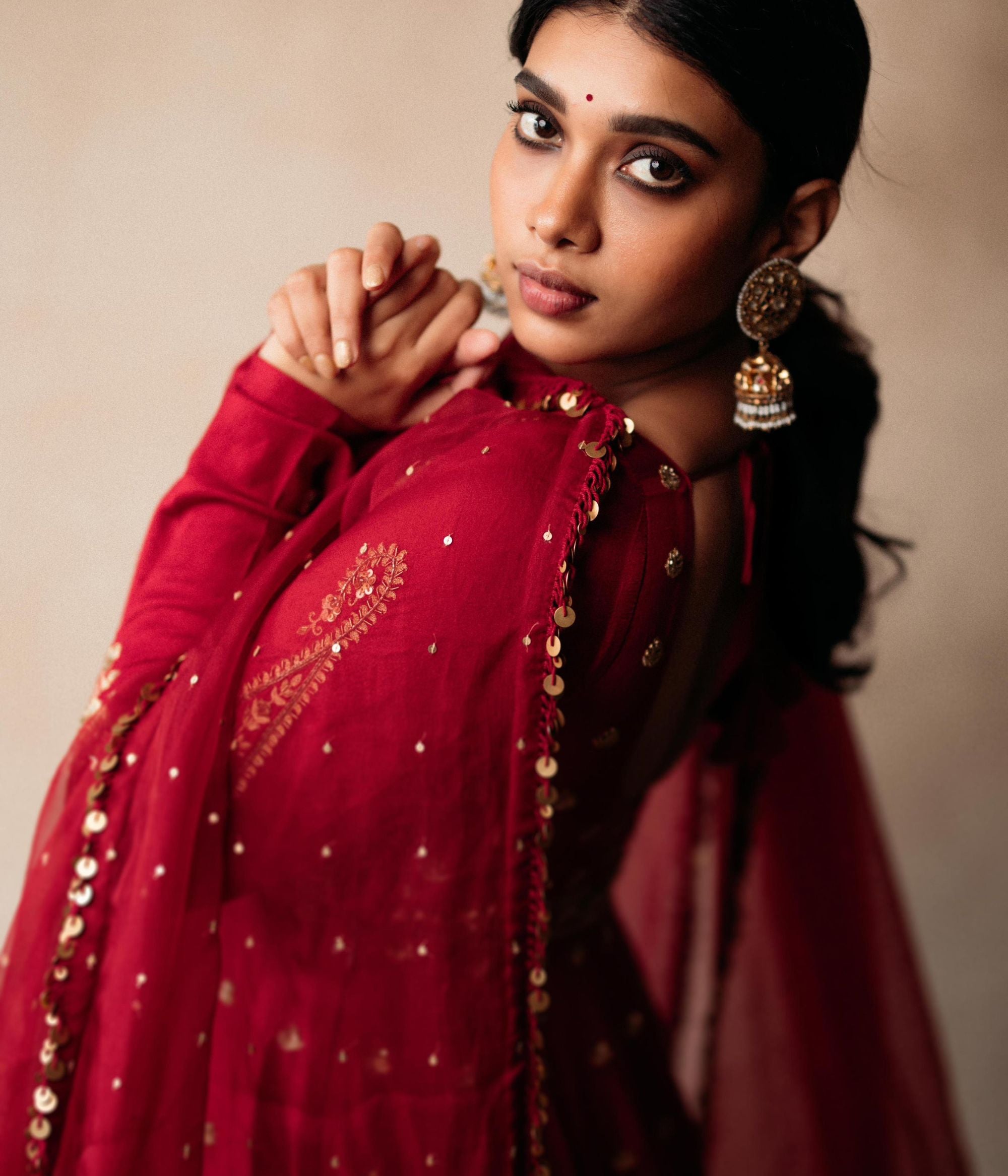 Large gold jhumka earrings with white sapphires, rubies, and pearls, on a woman wearing a red sari.