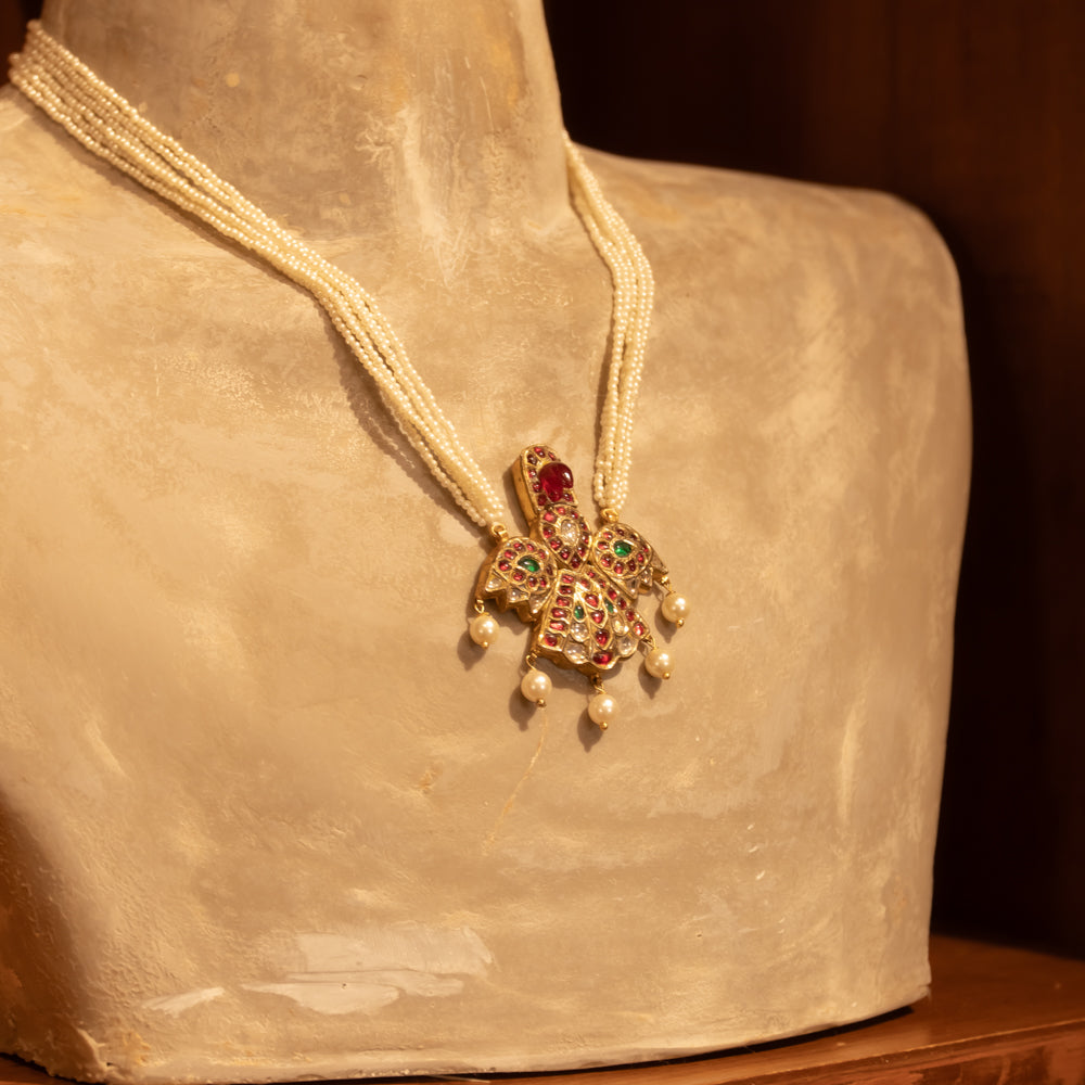 Multi-strand pearl necklace with a central gold pendant featuring rubies and white sapphires, displayed on a mannequin bust.