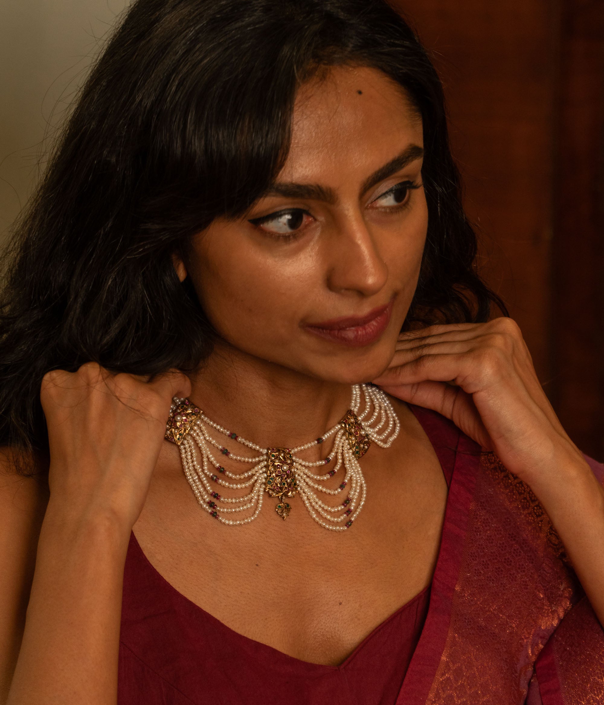 Multi-strand pearl necklace with a central gold pendant featuring rubies and white sapphires, worn by a woman.