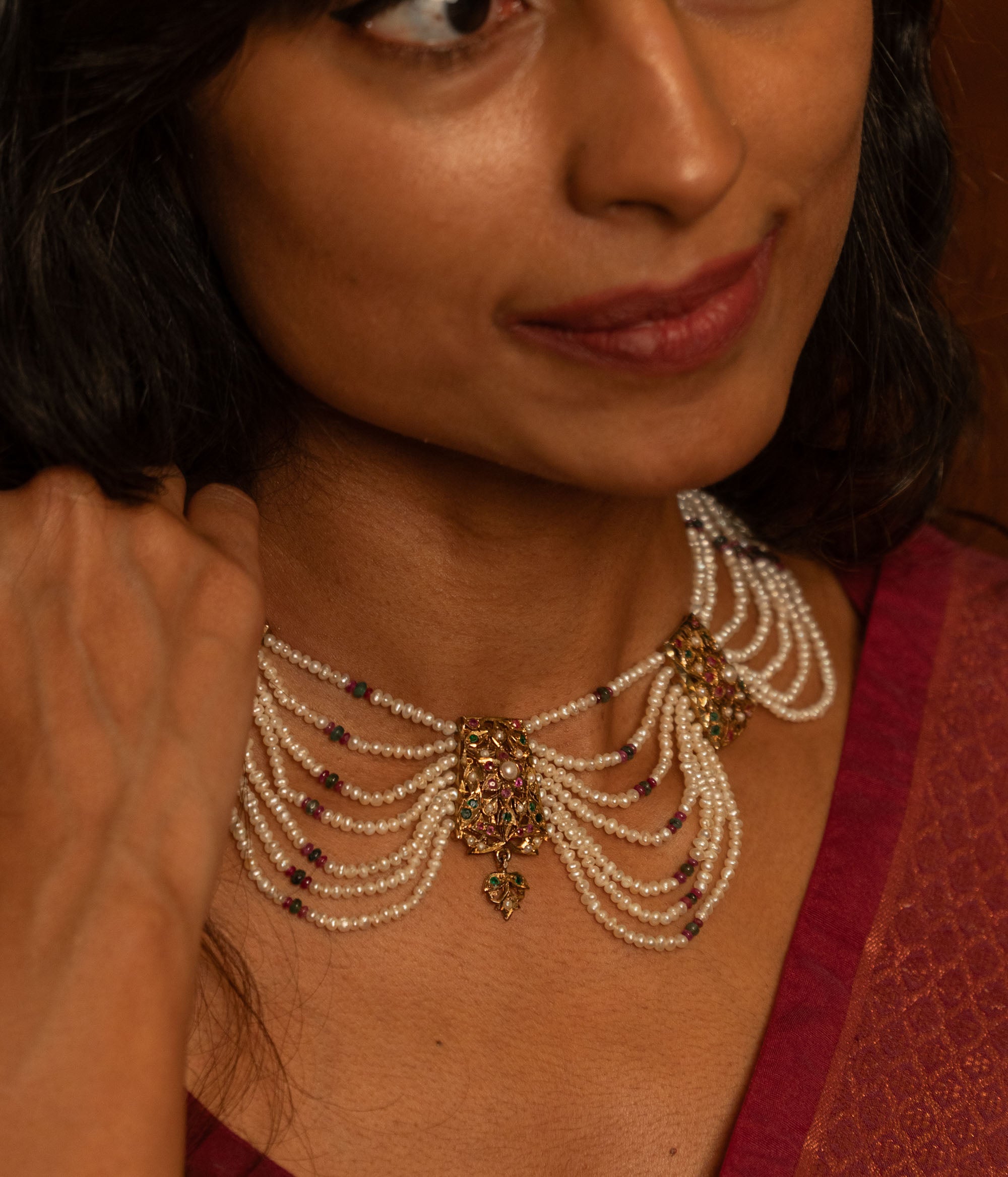 Multi-strand pearl necklace with a central gold pendant featuring rubies and white sapphires, worn by a woman.