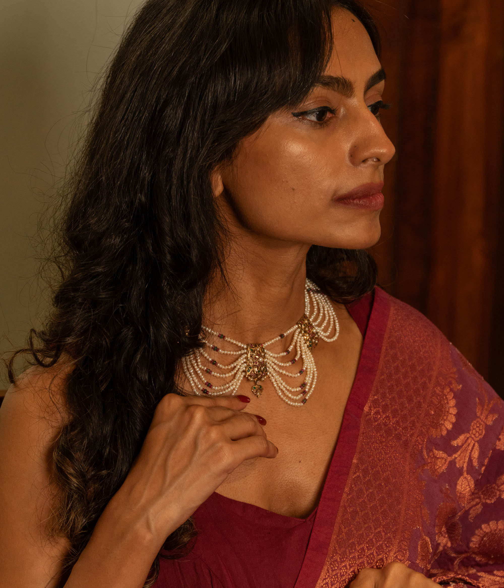 Multi-strand pearl necklace with a central gold pendant featuring rubies and white sapphires, worn by a woman.