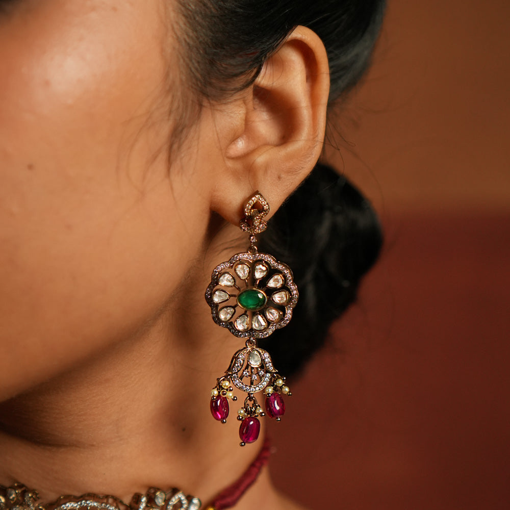 Gold-plated floral dangler earring featuring Green Gemstone, Moissanite Polki Stones, Pearls, Red Beads, and CZ Stones. The earring has a floral design with Polki and CZ stones arranged around it, complemented by delicate drops of red beads for an elegant finish.