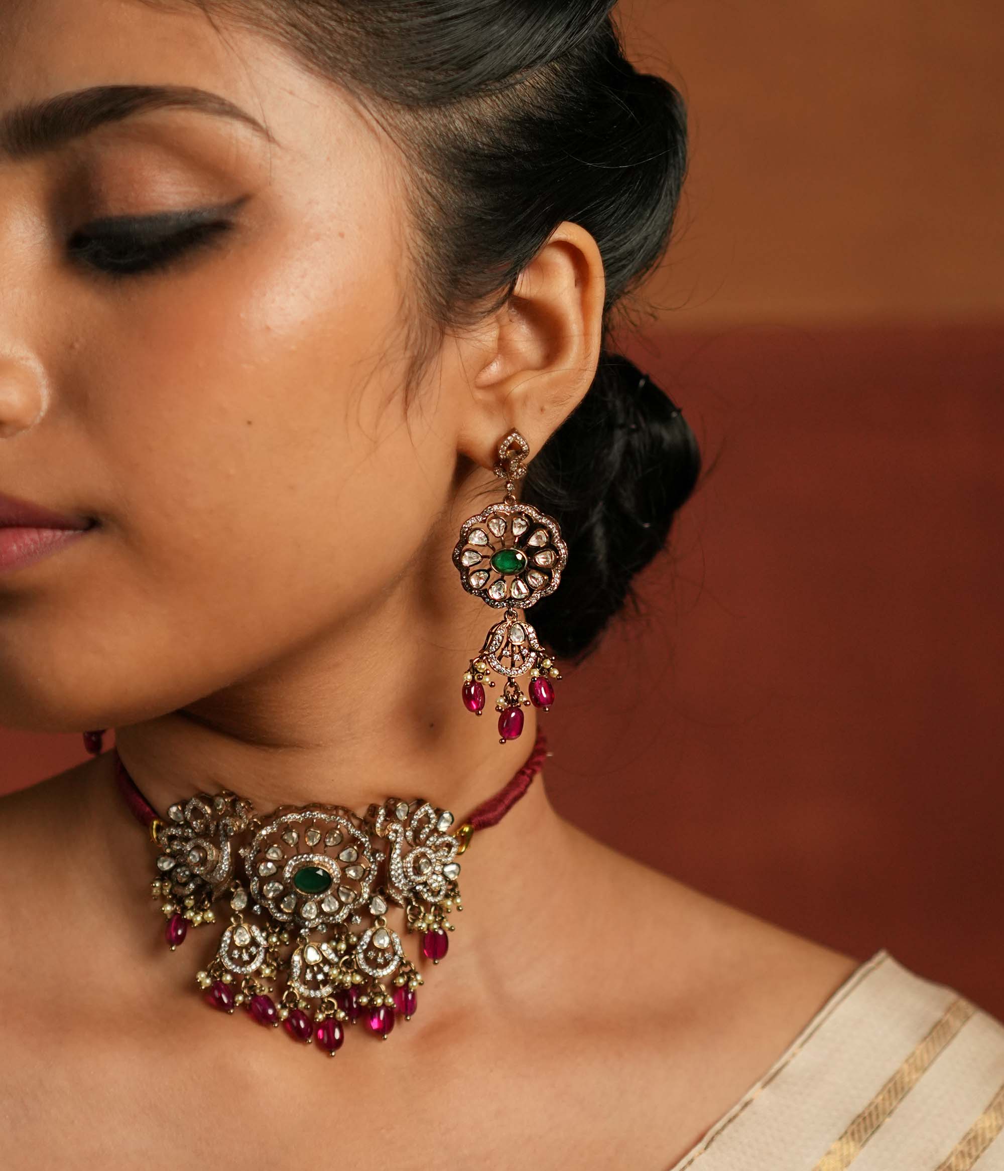 Gold-plated floral dangler earring featuring Green Gemstone, Moissanite Polki Stones, Pearls, Red Beads, and CZ Stones. The earring has a floral design with Polki and CZ stones arranged around it, complemented by delicate drops of red beads for an elegant finish.