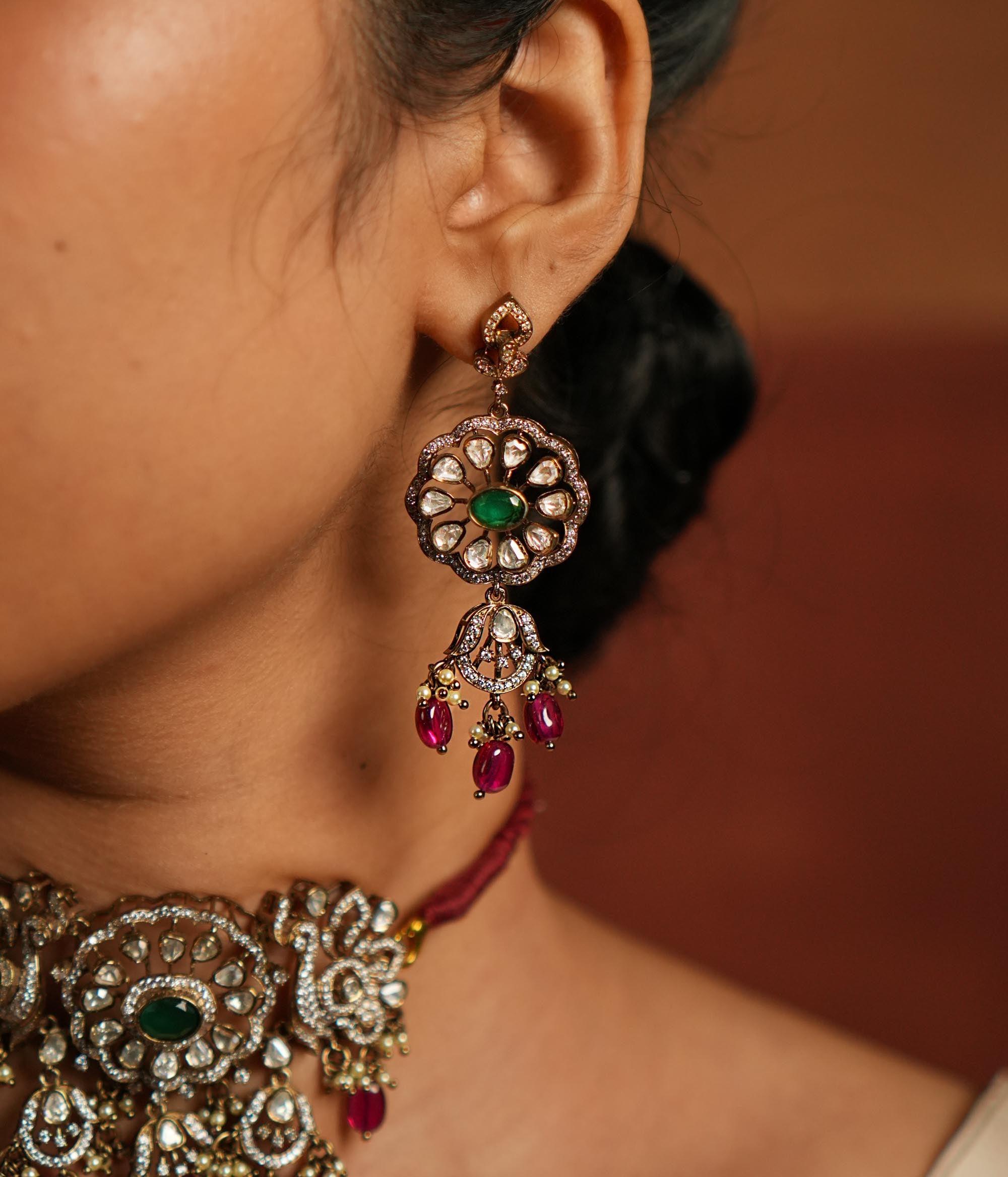Gold-plated floral dangler earring featuring Green Gemstone, Moissanite Polki Stones, Pearls, Red Beads, and CZ Stones. The earring has a floral design with Polki and CZ stones arranged around it, complemented by delicate drops of red beads for an elegant finish.
