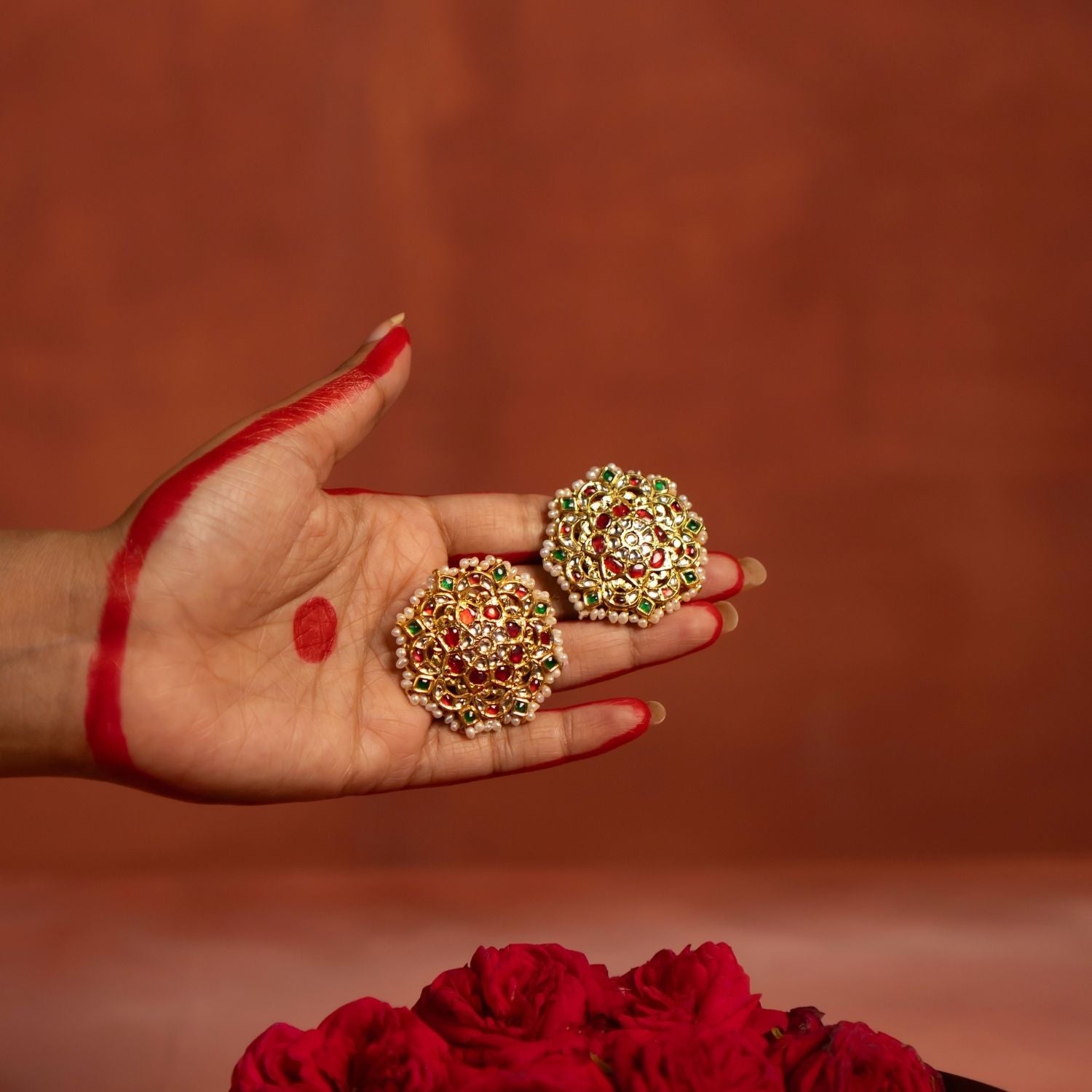 A beautifully crafted gold-plated silver push-type stud earring in a round floral design. Adorned with vibrant rubies, sparkling white sapphires, rich emeralds, and elegant white pearls, this earring exudes a traditional charm, making it a perfect accessory for ethnic and festive occasions.