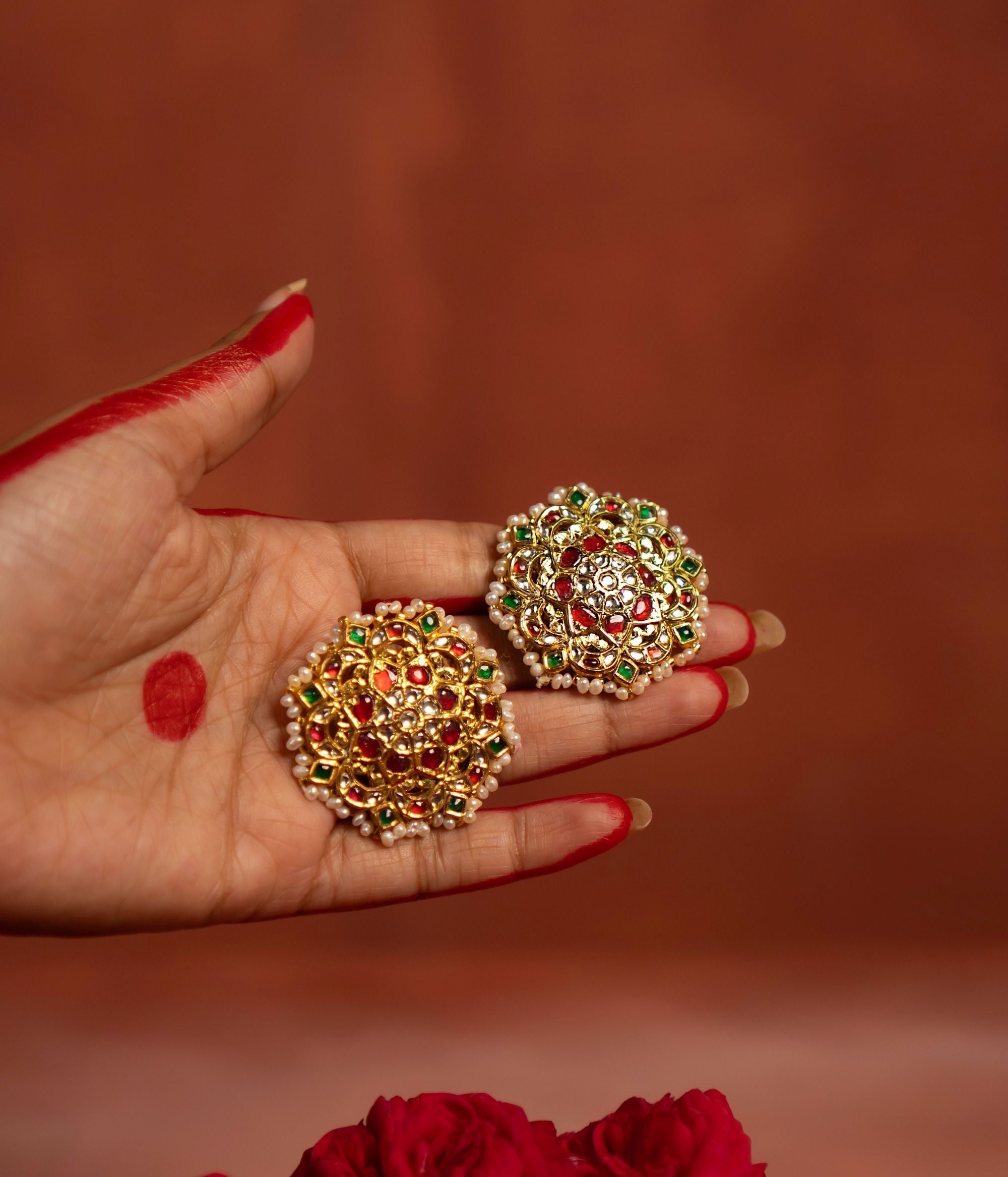 A beautifully crafted gold-plated silver push-type stud earring in a round floral design. Adorned with vibrant rubies, sparkling white sapphires, rich emeralds, and elegant white pearls, this earring exudes a traditional charm, making it a perfect accessory for ethnic and festive occasions.