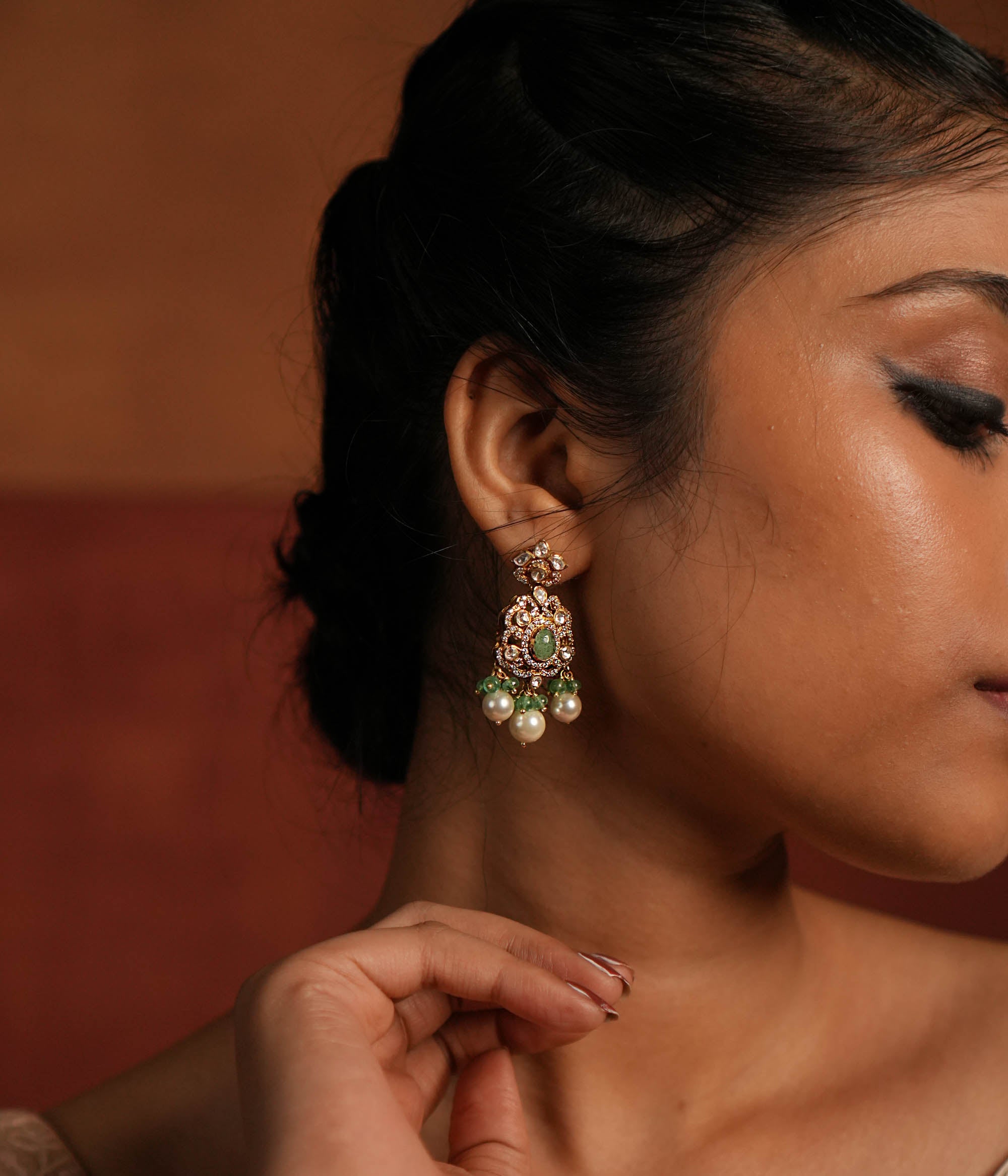 Exquisite gold-plated silver dangler earrings featuring a floral stud with a dazzling Polki stone at the center, encased in shimmering CZ stones. The elegant drop showcases a vibrant green gemstone in the middle, surrounded by Polki and CZ stones, forming a graceful floral design. Delicate white pearl and green bead drops enhance its charm, adding a touch of sophistication and tradition to any look.