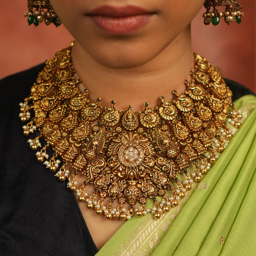 An antique gold-plated temple necklace adorned with intricate peacock motifs and delicate pearl droplets evokes timeless opulence—a divine treasure whispering elegance for the modern bride.