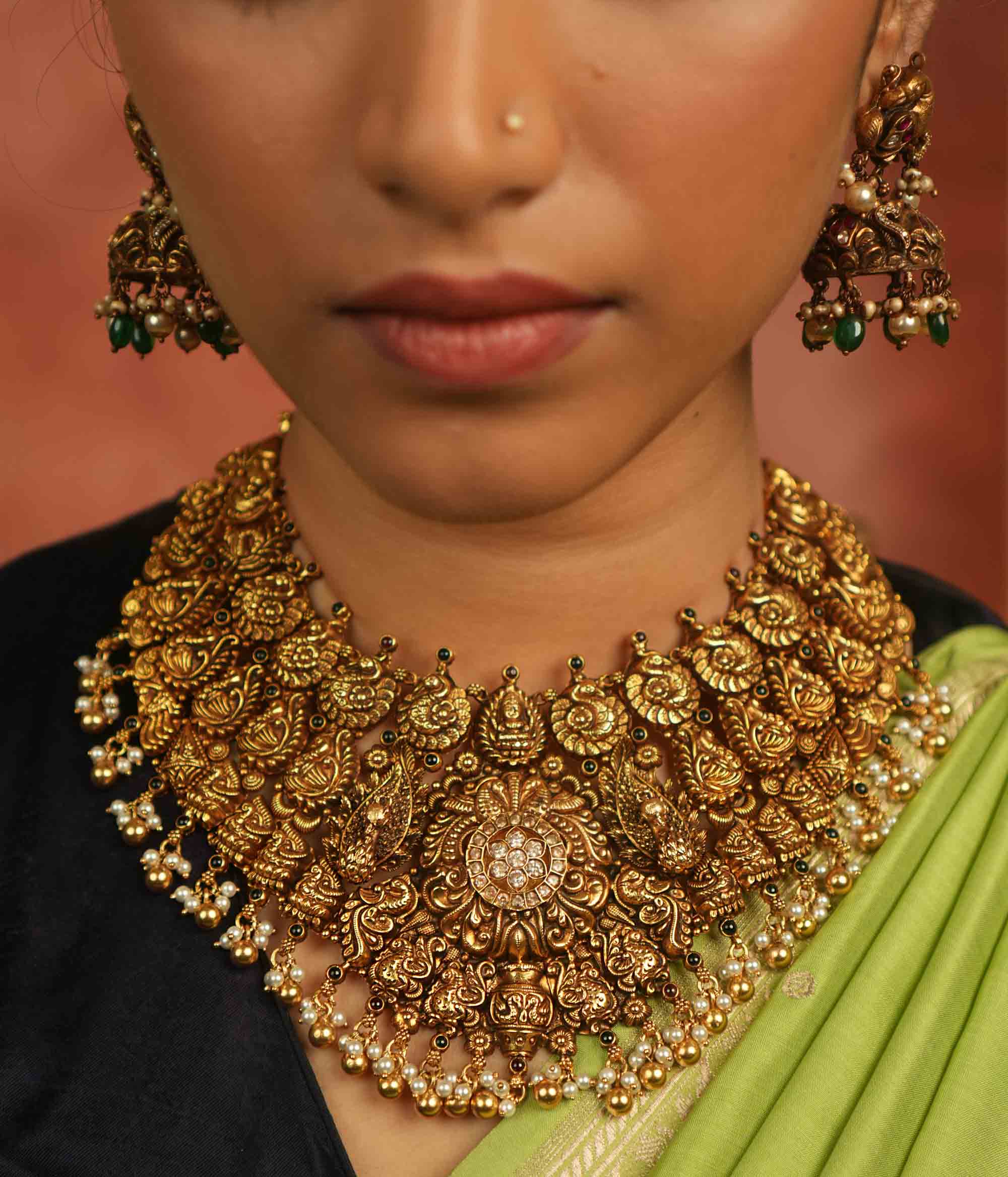 An antique gold-plated temple necklace adorned with intricate peacock motifs and delicate pearl droplets evokes timeless opulence—a divine treasure whispering elegance for the modern bride.