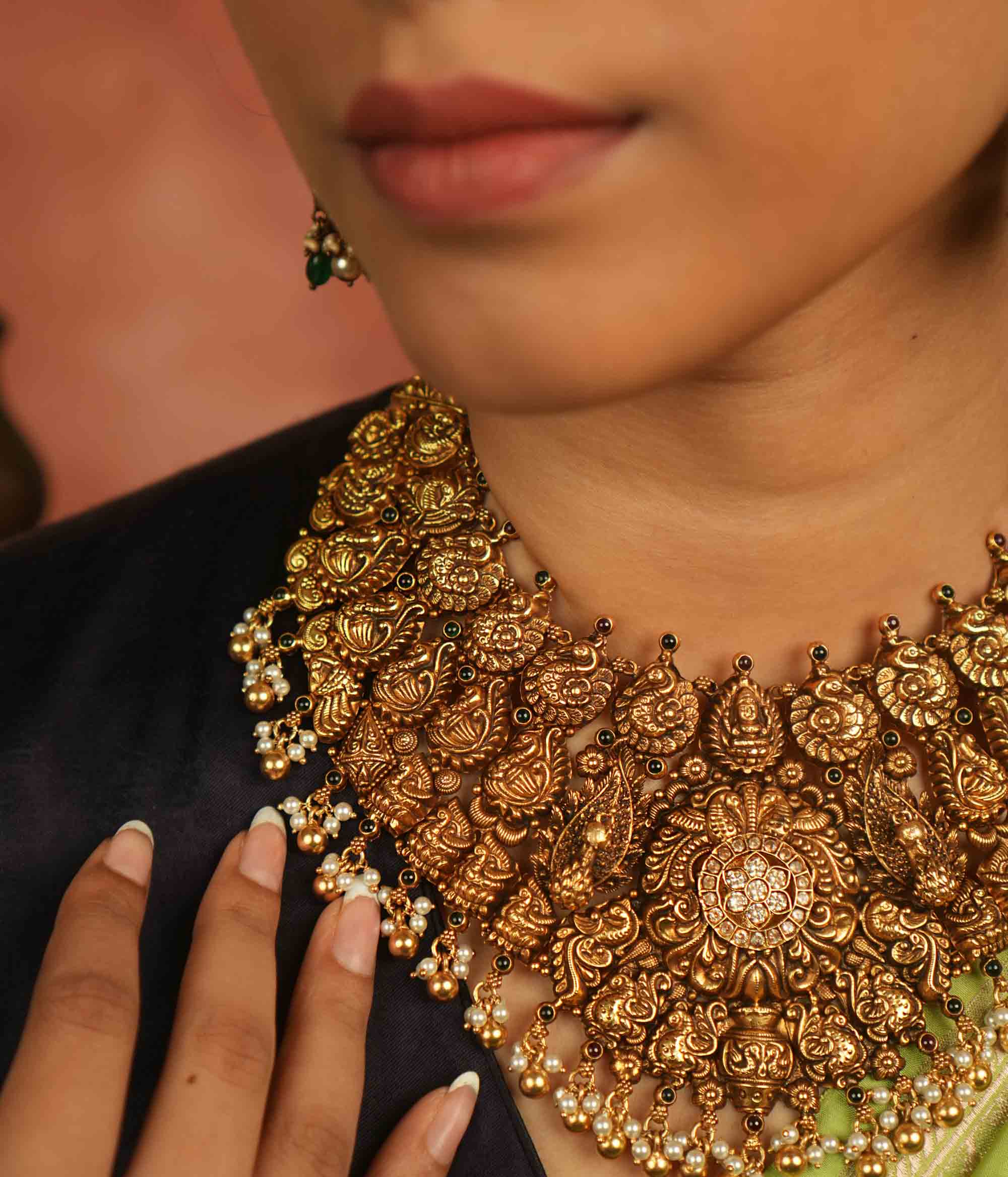 An antique gold-plated temple necklace adorned with intricate peacock motifs and delicate pearl droplets evokes timeless opulence—a divine treasure whispering elegance for the modern bride.