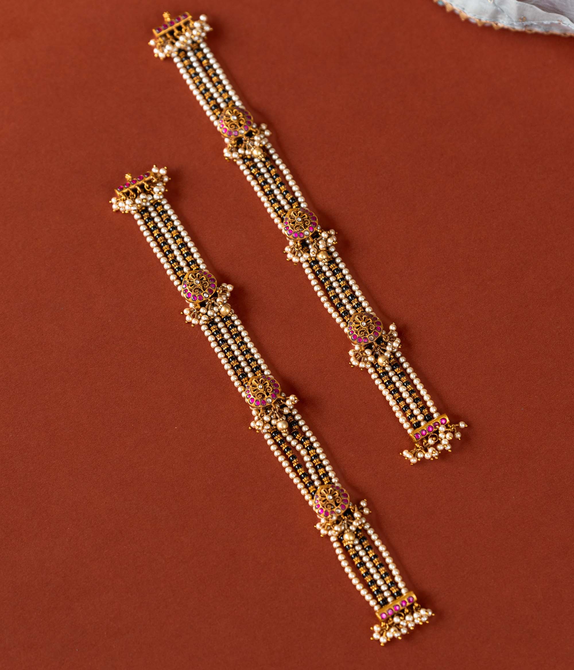 Handcrafted chain made of 92.5 sterling silver and 22 carat gold plating, featuring red and white Kundan stones and pearls. The design includes vibrant beads, intricate gold detailing, and delicate pearl drops, blending tradition with graceful elegance