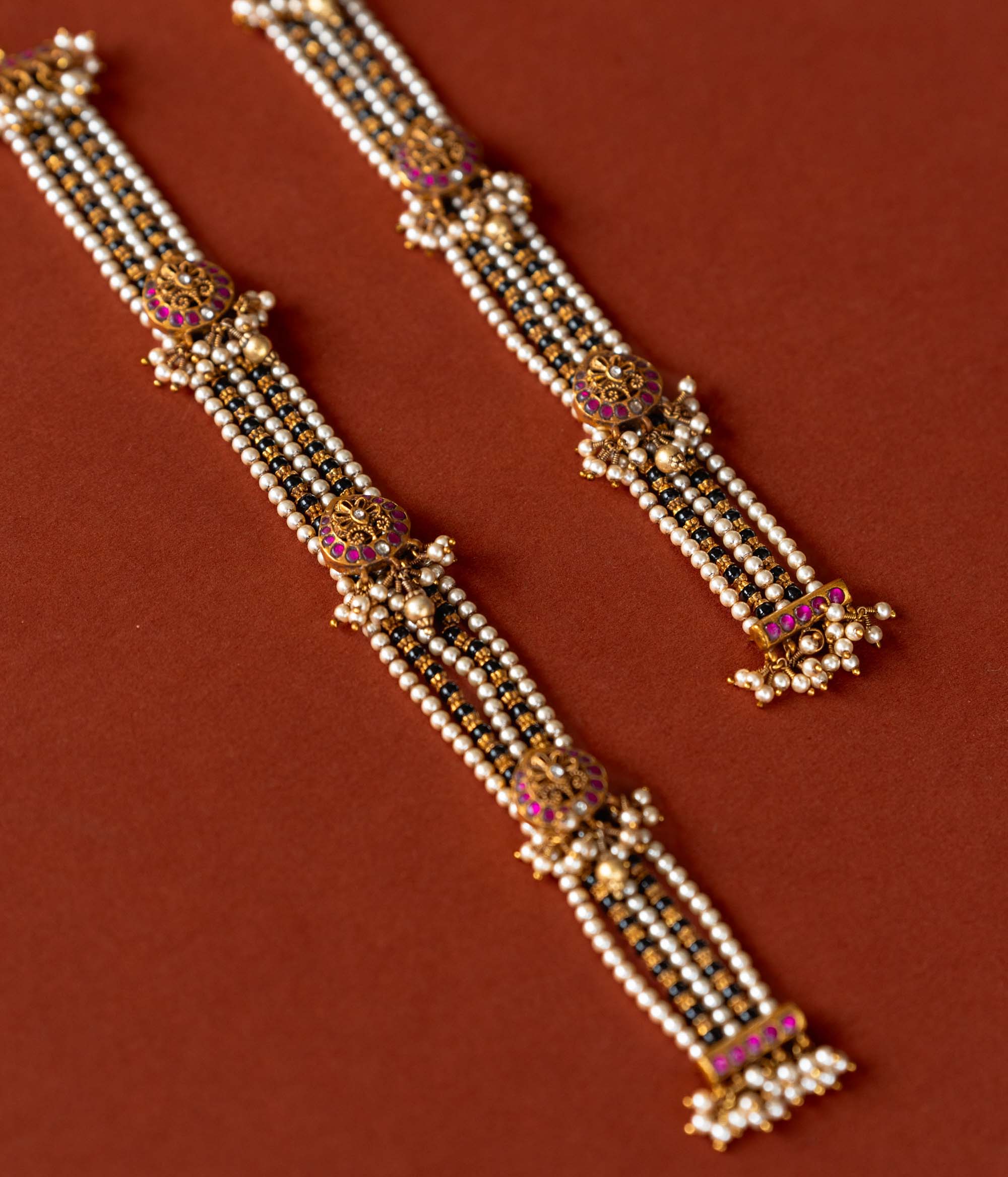 Handcrafted chain made of 92.5 sterling silver and 22 carat gold plating, featuring red and white Kundan stones and pearls. The design includes vibrant beads, intricate gold detailing, and delicate pearl drops, blending tradition with graceful elegance