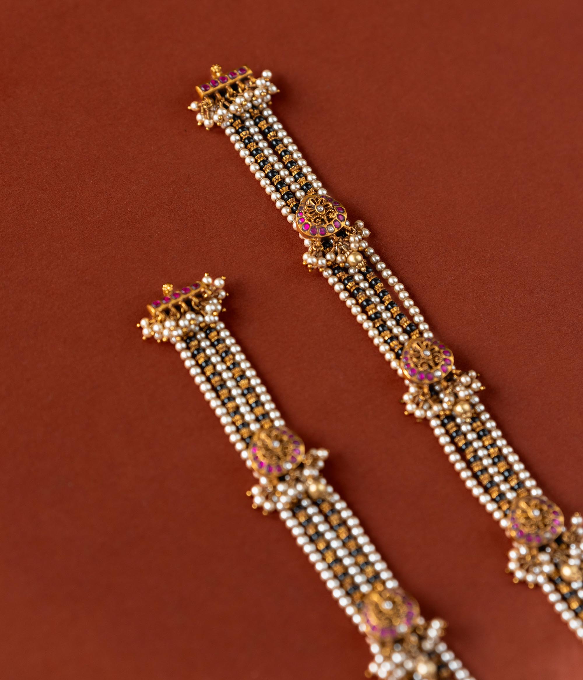 Handcrafted chain made of 92.5 sterling silver and 22 carat gold plating, featuring red and white Kundan stones and pearls. The design includes vibrant beads, intricate gold detailing, and delicate pearl drops, blending tradition with graceful elegance
