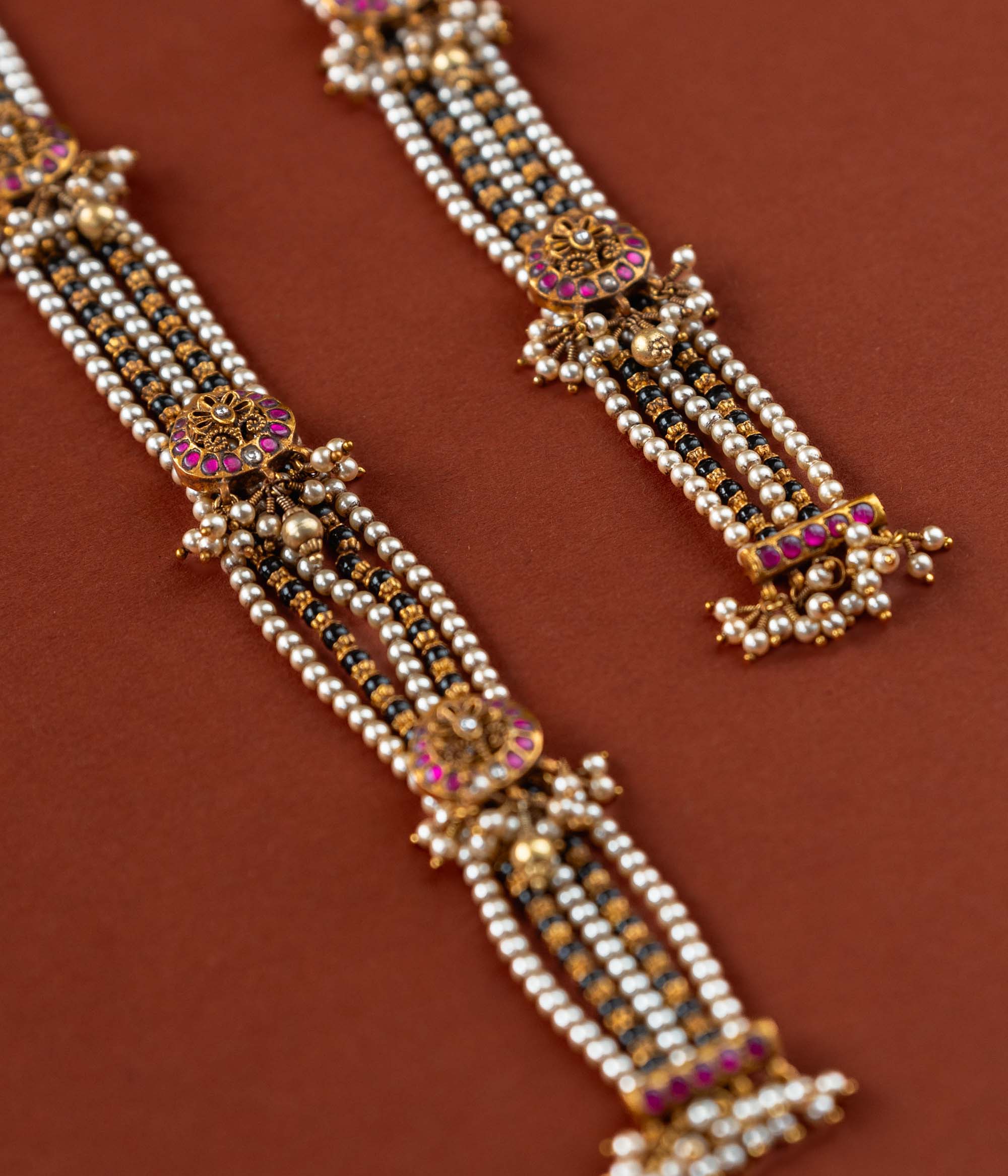 Handcrafted chain made of 92.5 sterling silver and 22 carat gold plating, featuring red and white Kundan stones and pearls. The design includes vibrant beads, intricate gold detailing, and delicate pearl drops, blending tradition with graceful elegance