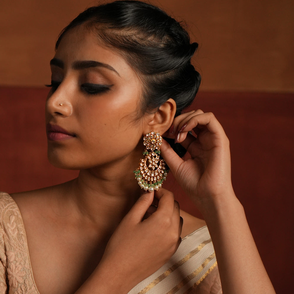 Exquisite gold-plated silver dangler earrings featuring a stunning floral design adorned with shimmering Polki and CZ stones. The elegant drops are embellished with delicate white pearls and vibrant green beads, adding a graceful and timeless charm. A perfect blend of tradition and elegance, these earrings are ideal for any occasion.