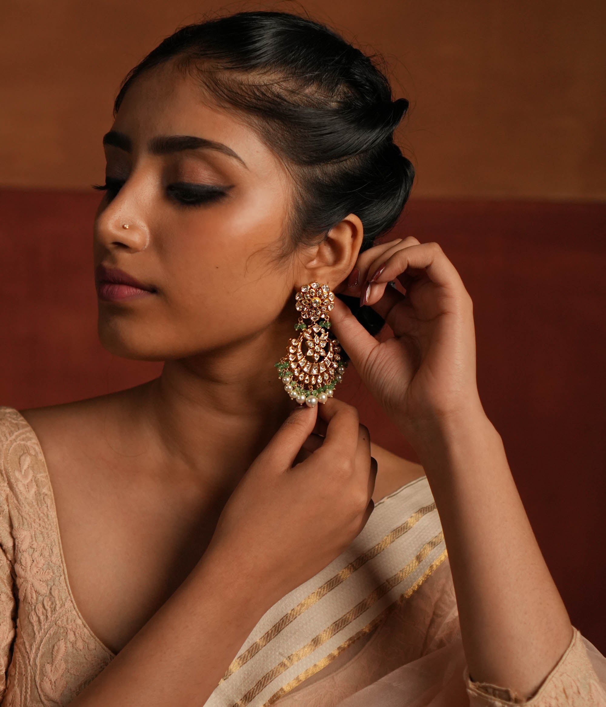 Exquisite gold-plated silver dangler earrings featuring a stunning floral design adorned with shimmering Polki and CZ stones. The elegant drops are embellished with delicate white pearls and vibrant green beads, adding a graceful and timeless charm. A perfect blend of tradition and elegance, these earrings are ideal for any occasion.