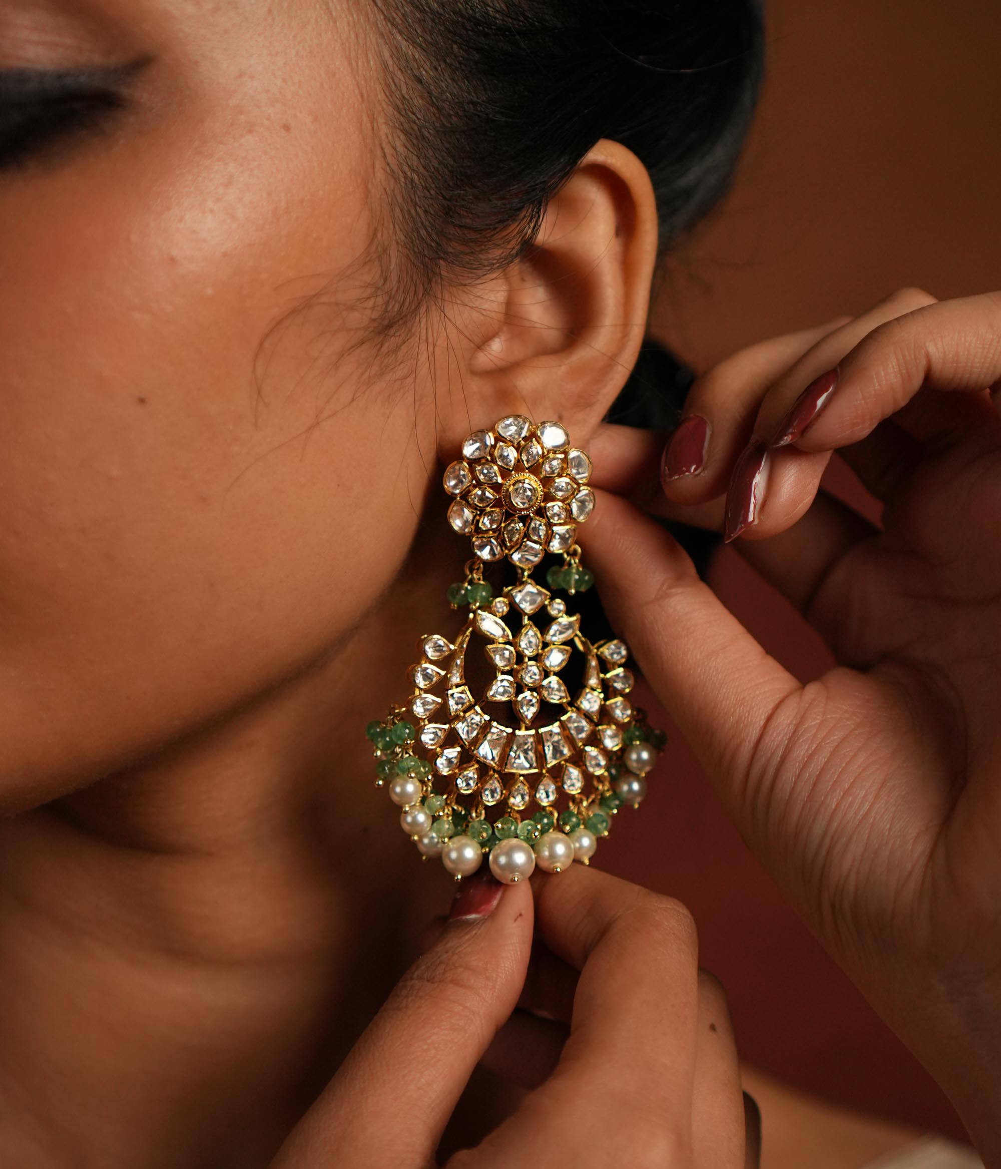 Exquisite gold-plated silver dangler earrings featuring a stunning floral design adorned with shimmering Polki and CZ stones. The elegant drops are embellished with delicate white pearls and vibrant green beads, adding a graceful and timeless charm. A perfect blend of tradition and elegance, these earrings are ideal for any occasion.