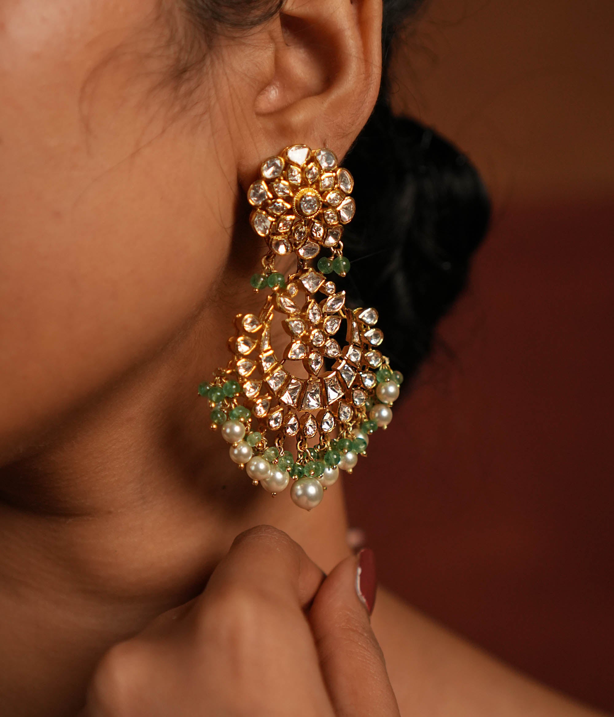 Exquisite gold-plated silver dangler earrings featuring a stunning floral design adorned with shimmering Polki and CZ stones. The elegant drops are embellished with delicate white pearls and vibrant green beads, adding a graceful and timeless charm. A perfect blend of tradition and elegance, these earrings are ideal for any occasion.
