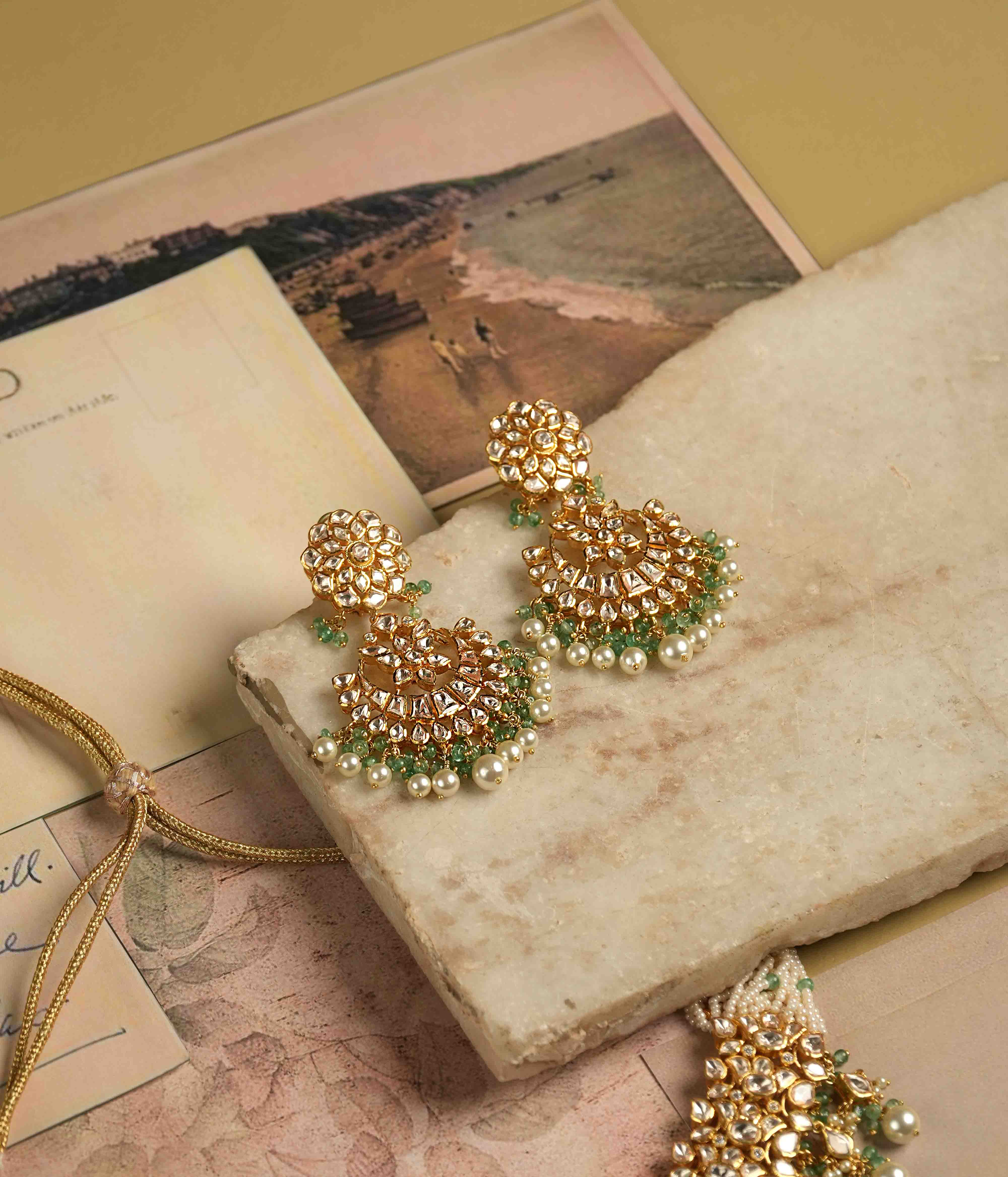 Exquisite gold-plated silver dangler earrings featuring a stunning floral design adorned with shimmering Polki and CZ stones. The elegant drops are embellished with delicate white pearls and vibrant green beads, adding a graceful and timeless charm. A perfect blend of tradition and elegance, these earrings are ideal for any occasion.