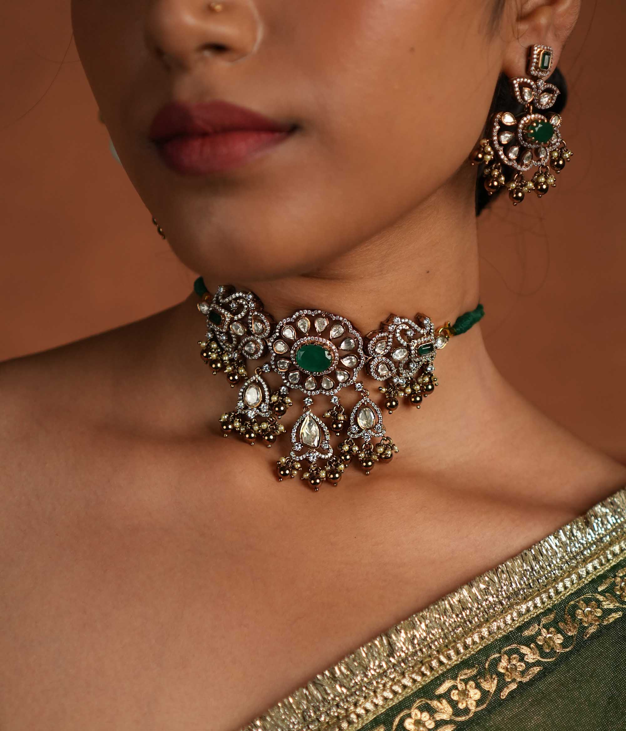 Victorian elegance reborn! This gold-plated silver choker features a striking green gemstone at its heart, surrounded by dazzling polki and CZ stones. Delicate pearl drops with golden beads enhance its timeless allure, whispering tales of a bygone era. A perfect blend of heritage and grace for the modern woman.