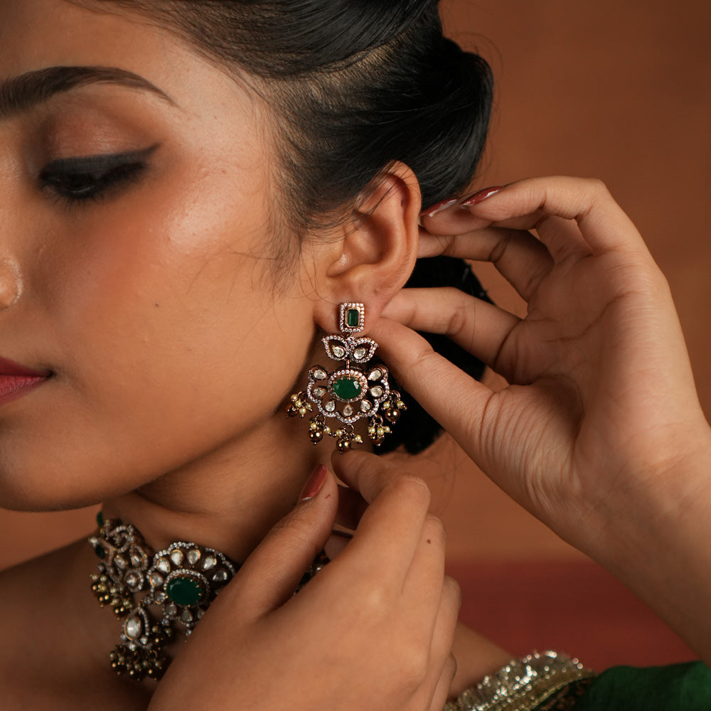 Victorian elegance reborn! These gold-plated silver Chandbali earrings showcase a radiant green gemstone at the center, encircled by shimmering polki and CZ stones. Graceful pearl drops with golden beads add a touch of charm, evoking the allure of a forgotten era. A secret garden of beauty, crafted to adorn the modern woman.