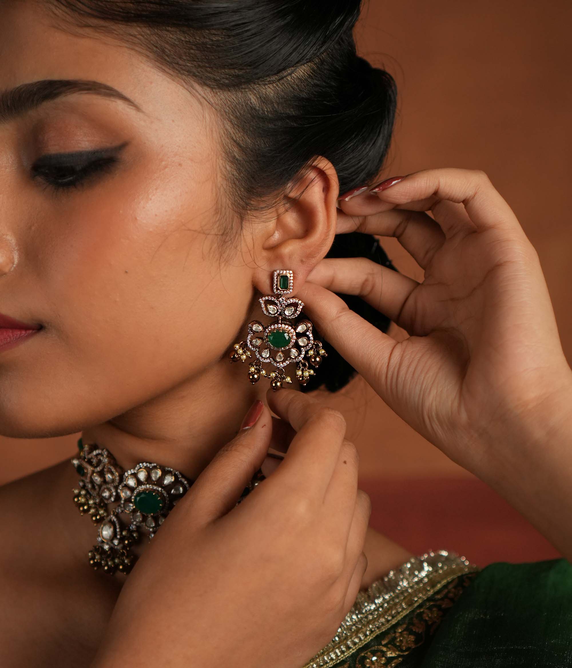 Victorian elegance reborn! These gold-plated silver Chandbali earrings showcase a radiant green gemstone at the center, encircled by shimmering polki and CZ stones. Graceful pearl drops with golden beads add a touch of charm, evoking the allure of a forgotten era. A secret garden of beauty, crafted to adorn the modern woman.