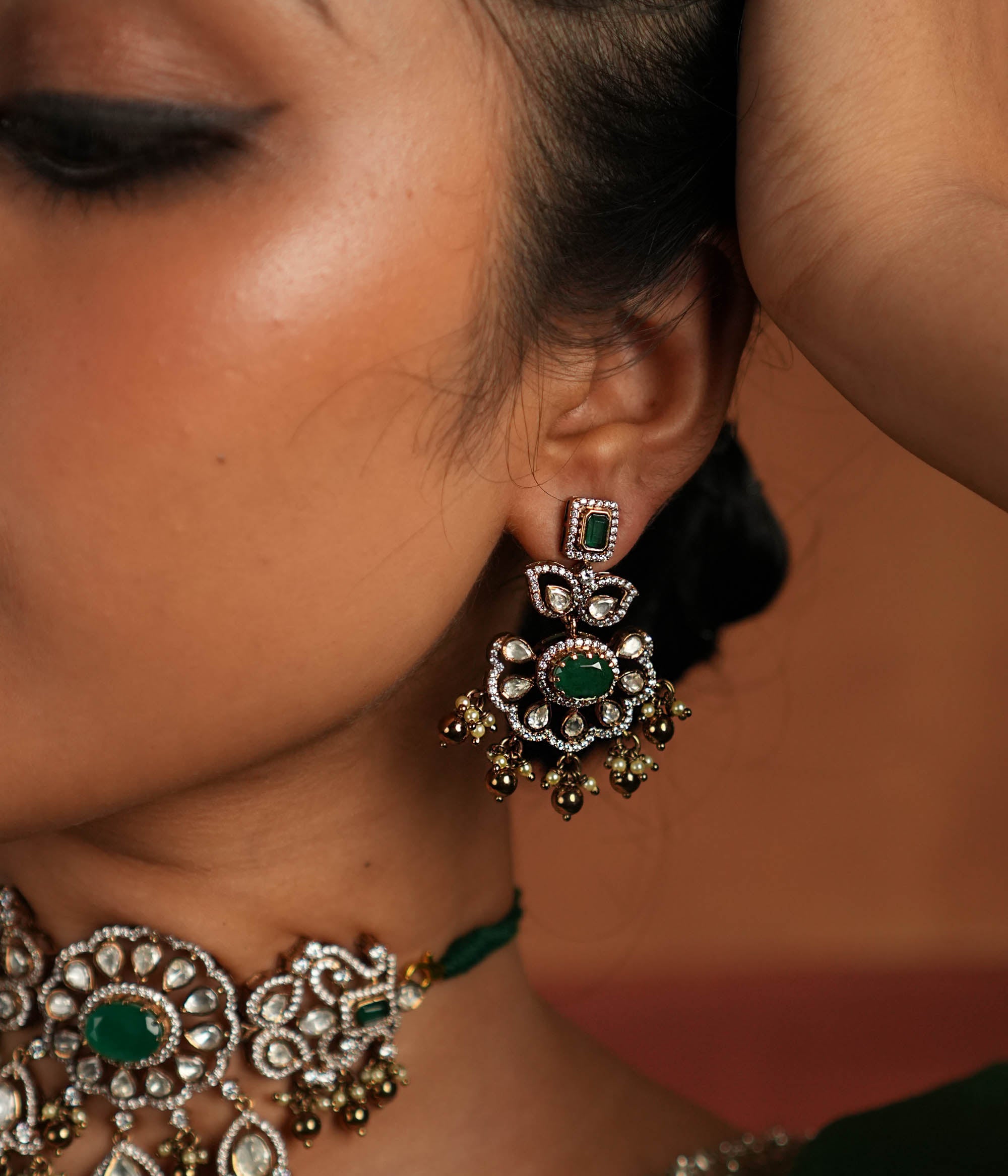 Victorian elegance reborn! These gold-plated silver Chandbali earrings showcase a radiant green gemstone at the center, encircled by shimmering polki and CZ stones. Graceful pearl drops with golden beads add a touch of charm, evoking the allure of a forgotten era. A secret garden of beauty, crafted to adorn the modern woman.