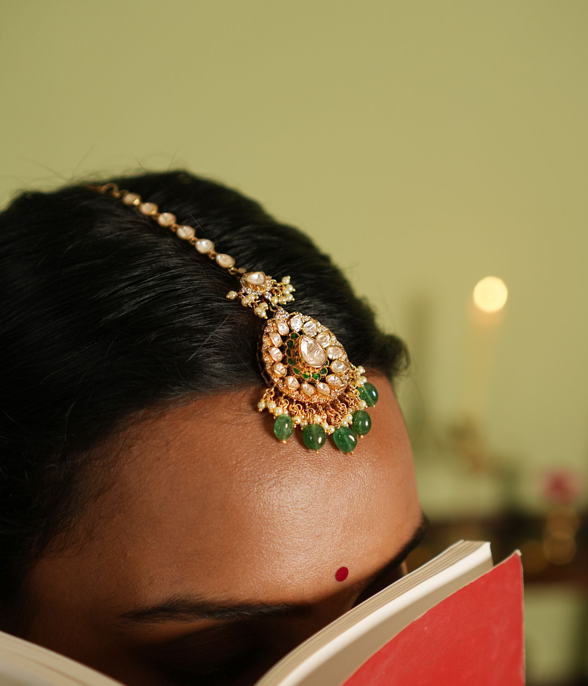 Victorian elegance reborn! This gold-plated silver maangtika features a stunning floral pendant with a central moissanite polki stone, encircled by smaller polkis and CZ stones. Graceful drops of green beads and pearls cascade beautifully, evoking whispers of forgotten lore. A timeless crown of sophistication, reimagined for the modern bride.