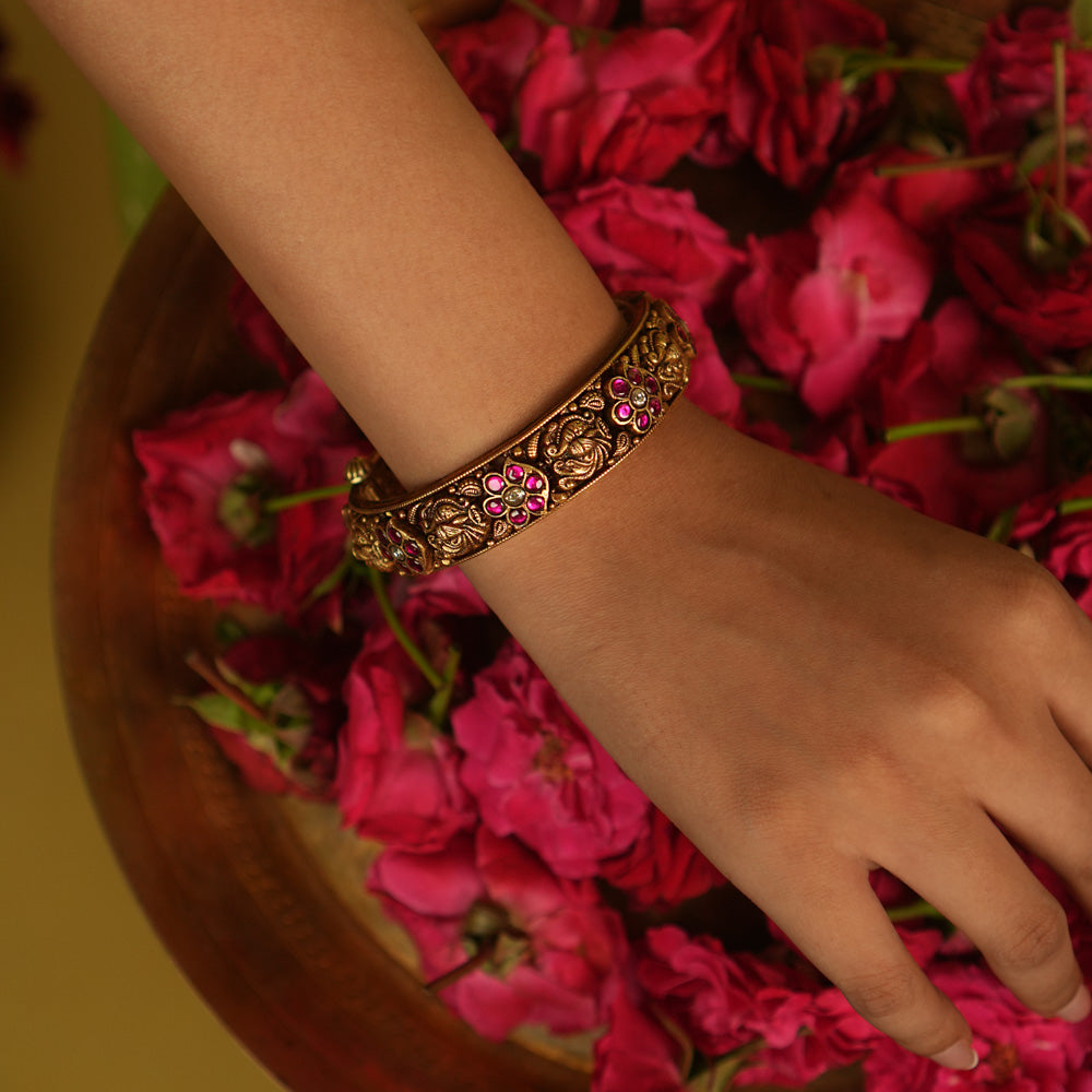 Temple whispers rekindled! An antique gold-plated bangle adorned with red and white kundan floral motifs and intricate temple designs narrates stories of timeless grace—a cherished jewel for the modern woman.