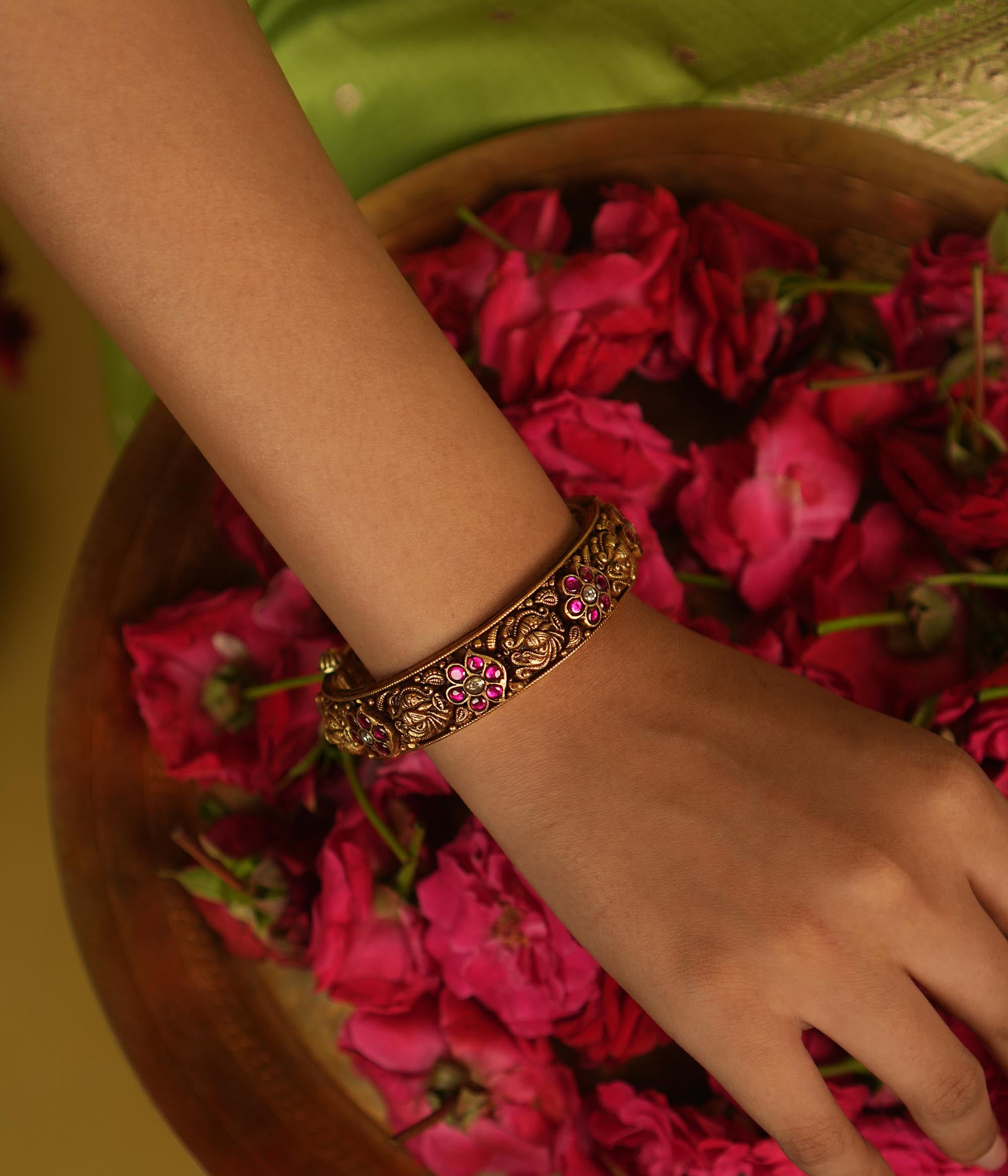 Temple whispers rekindled! An antique gold-plated bangle adorned with red and white kundan floral motifs and intricate temple designs narrates stories of timeless grace—a cherished jewel for the modern woman.