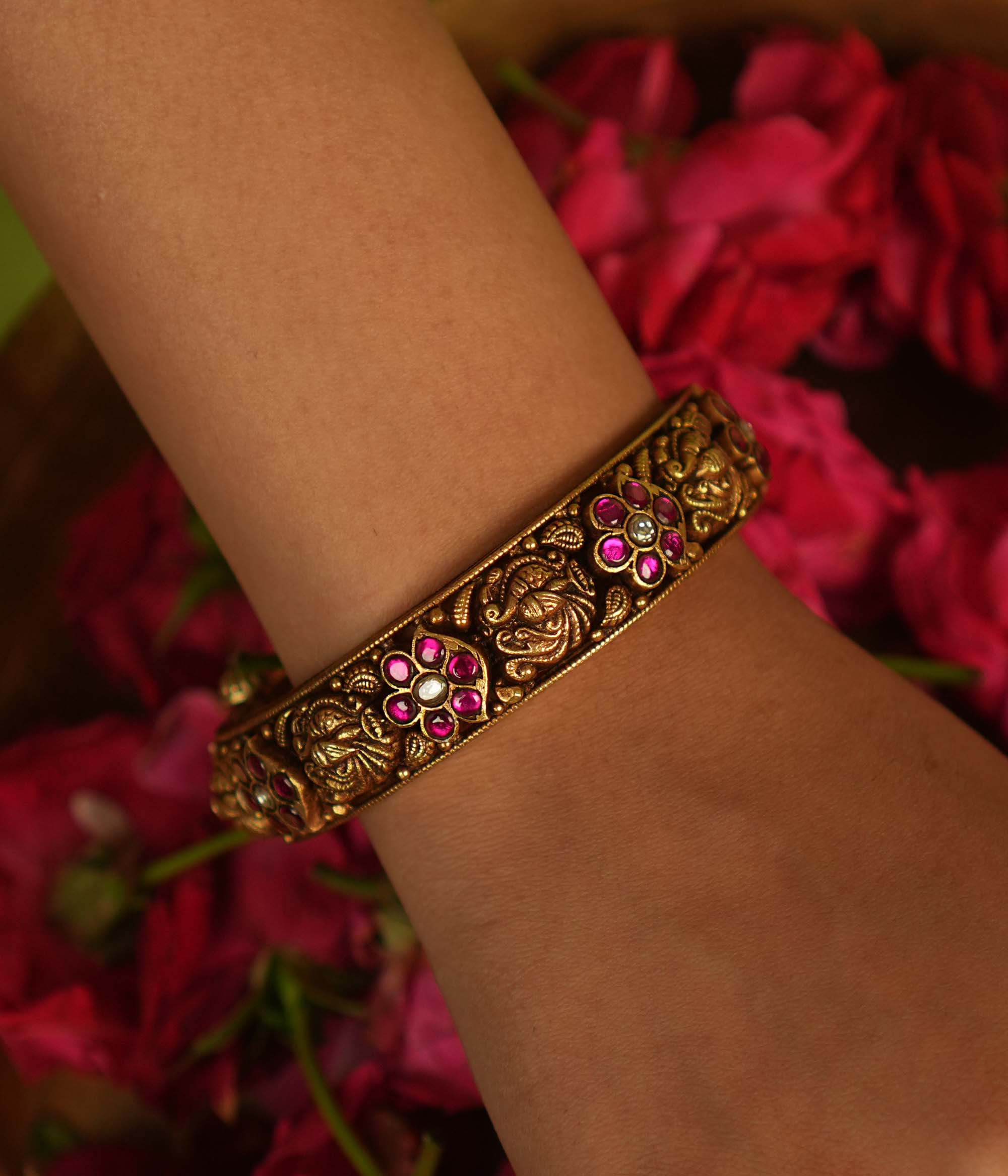 Temple whispers rekindled! An antique gold-plated bangle adorned with red and white kundan floral motifs and intricate temple designs narrates stories of timeless grace—a cherished jewel for the modern woman.