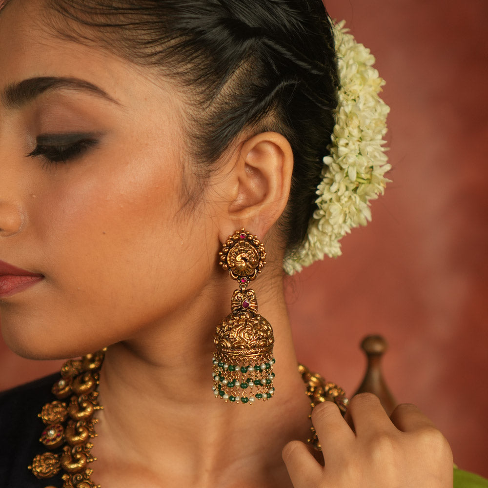 Mystic echoes reborn! Antique gold-plated jhumka adorned with red kundan, green and white bead droplets, exudes a peacock’s graceful opulence—an eternal treasure.