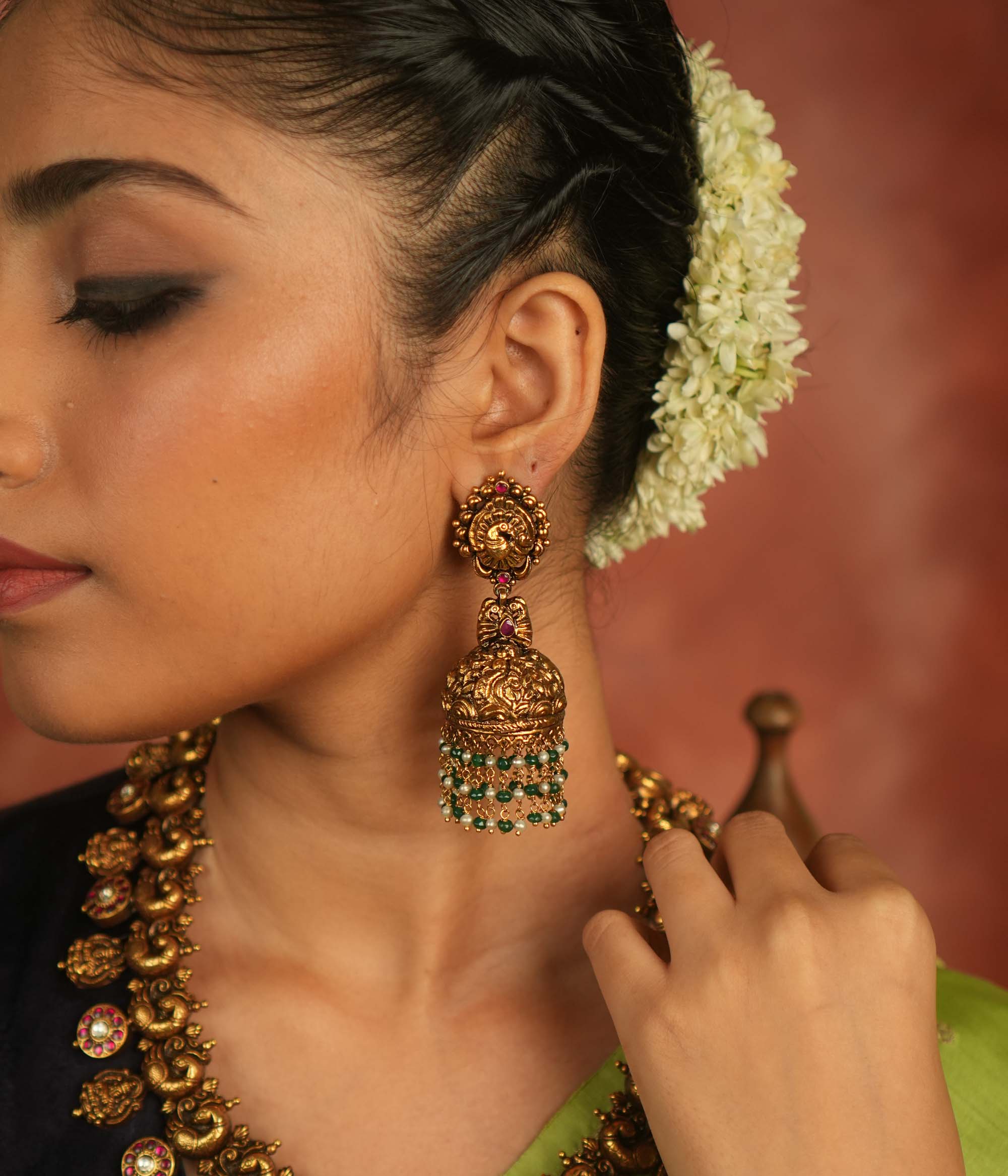 Mystic echoes reborn! Antique gold-plated jhumka adorned with red kundan, green and white bead droplets, exudes a peacock’s graceful opulence—an eternal treasure.